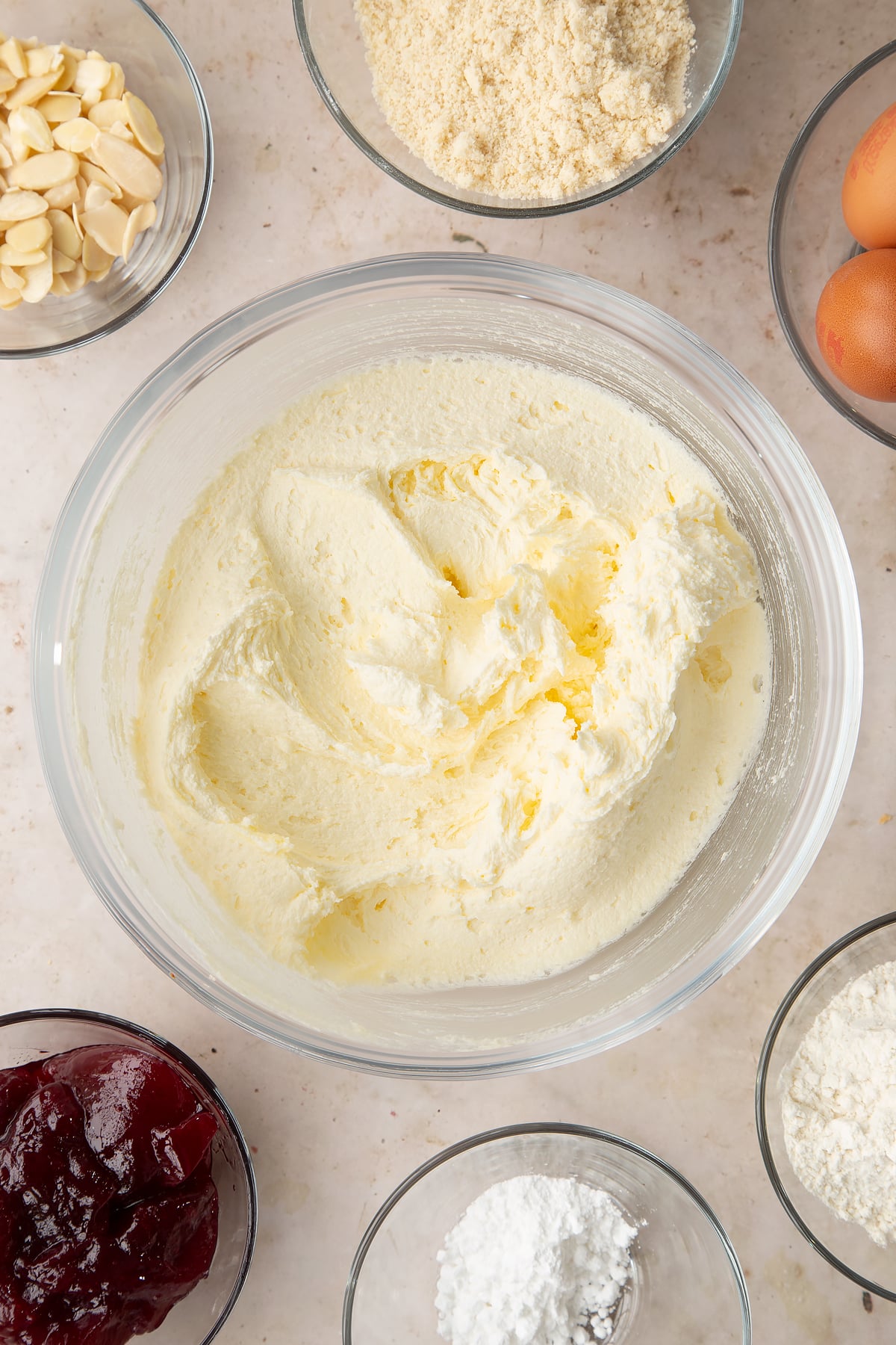 Butter and sugar creamed together in a bowl. Ingredients to make a Bakewell tray bake surround the bowl.
