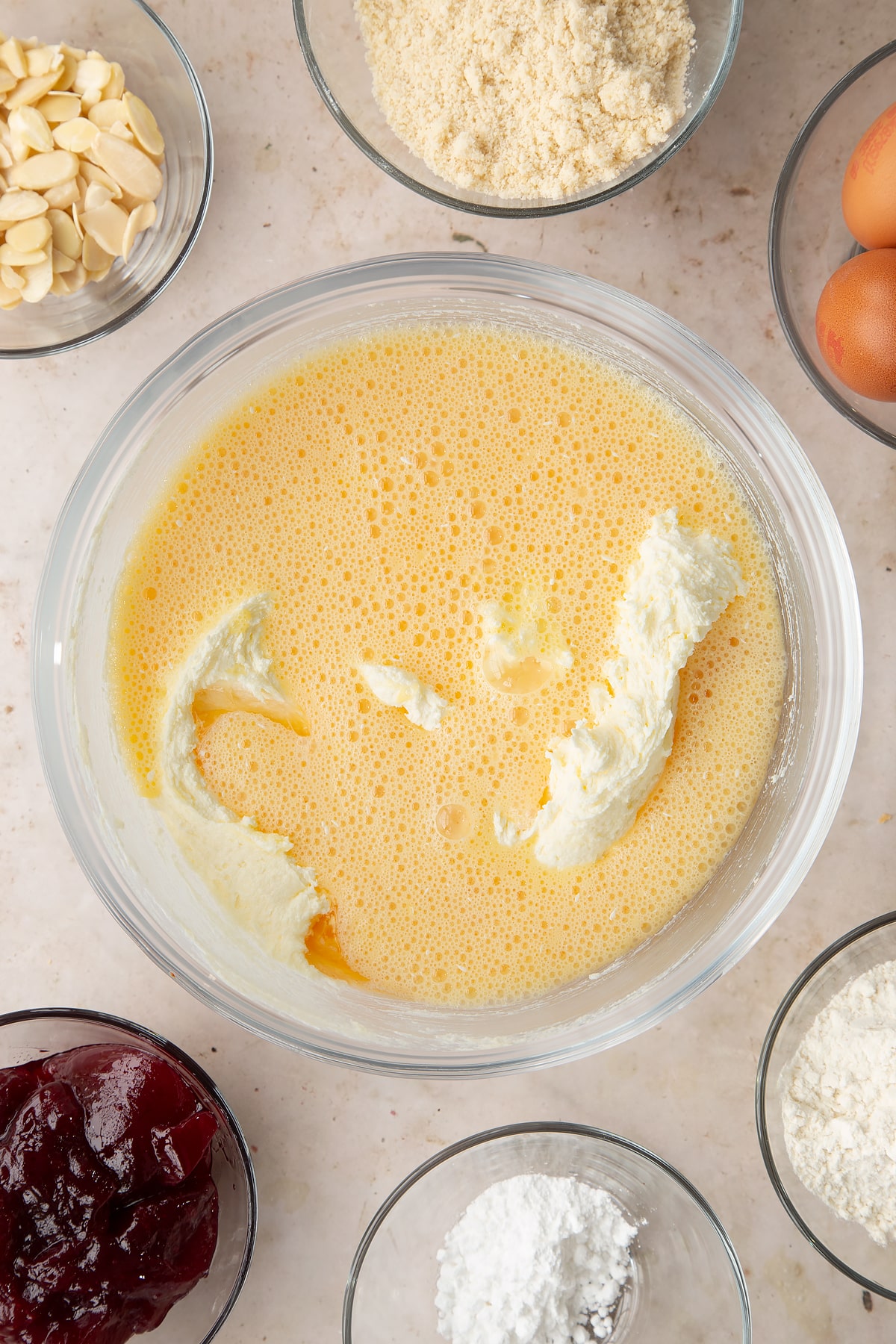Butter and sugar creamed together in a bowl with beaten eggs on top. Ingredients to make a Bakewell tray bake surround the bowl.