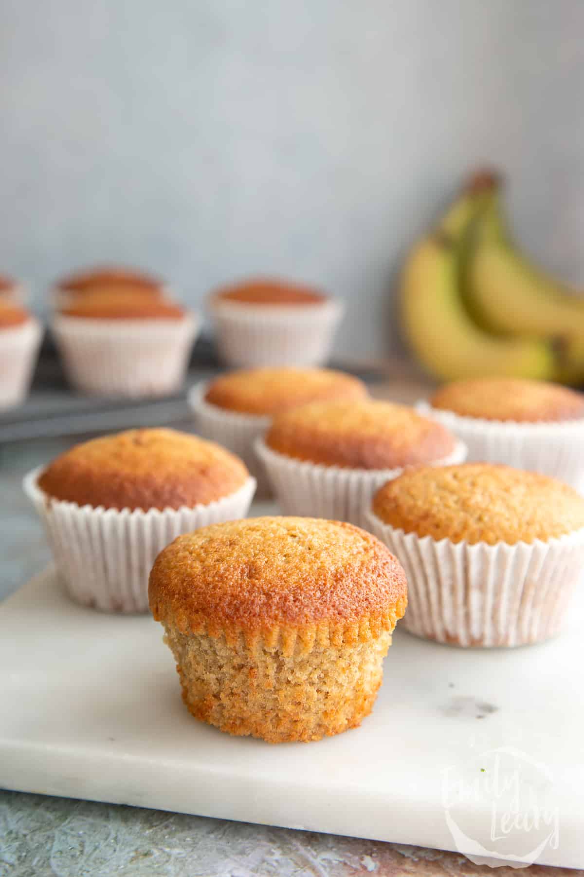 Banana cornmeal muffins on a white marble board. One has been unwrapped.