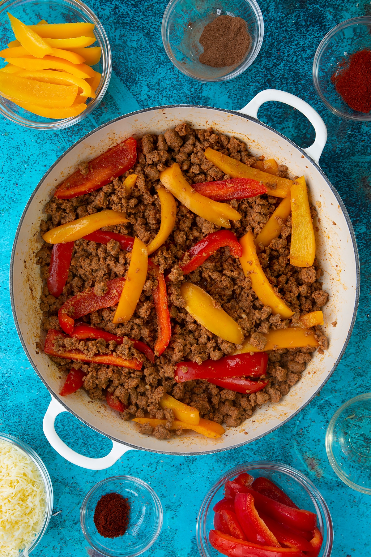 Quorn mince enchilada filling in a large white pan. Ingredients to make Quorn mince enchiladas surround the pan.