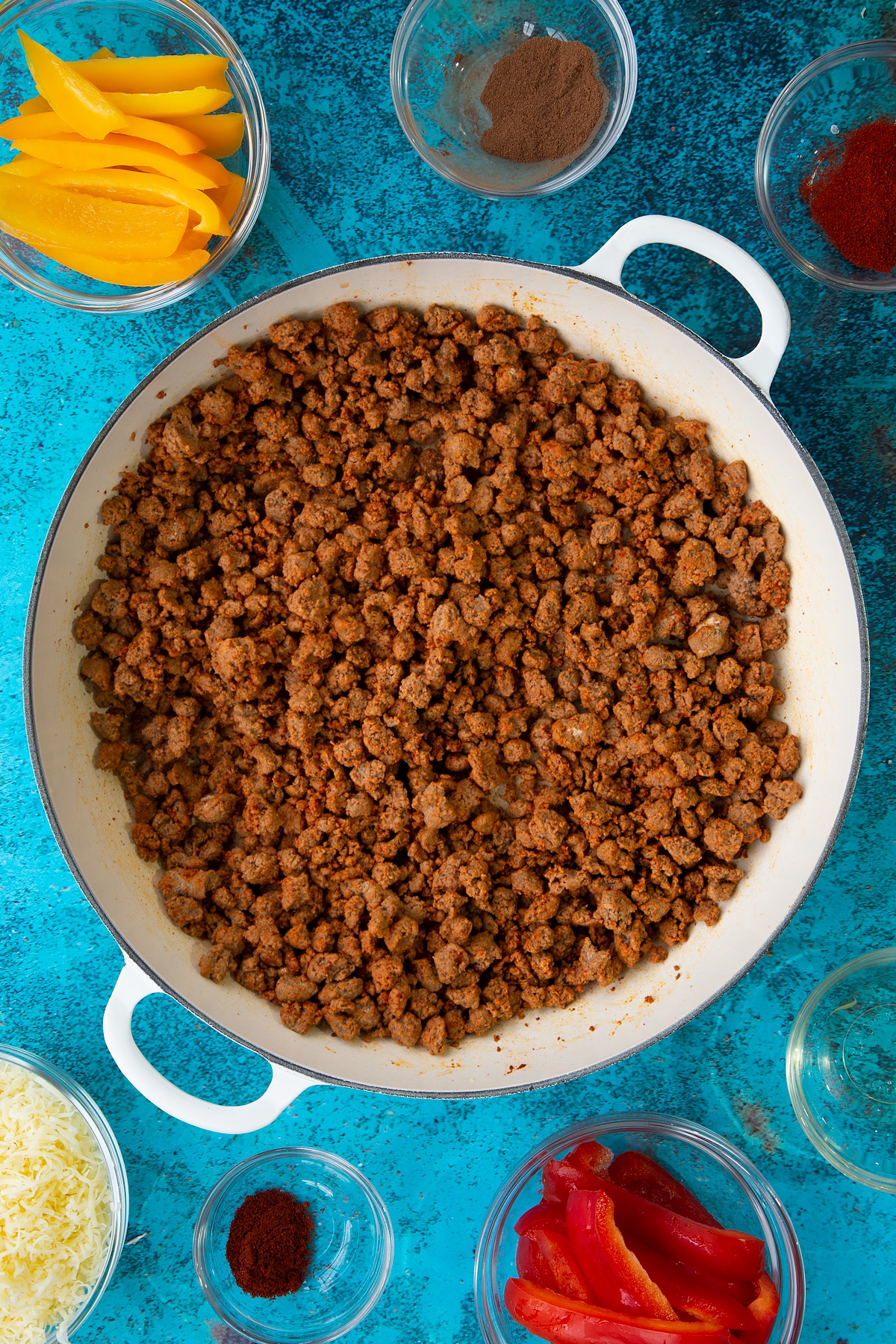 Quorn mince fried in spices in a large white pan. Ingredients to make Quorn mince enchiladas surround the pan.