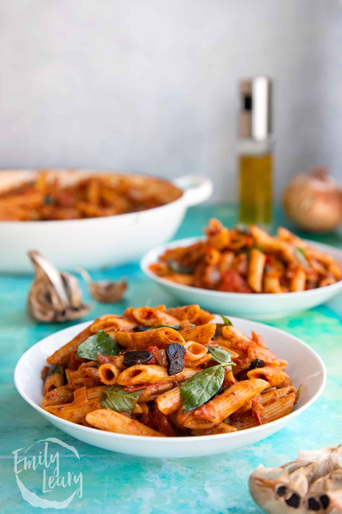 Two bowls of black garlic pasta with the dish of the black garlic pasta in the background.