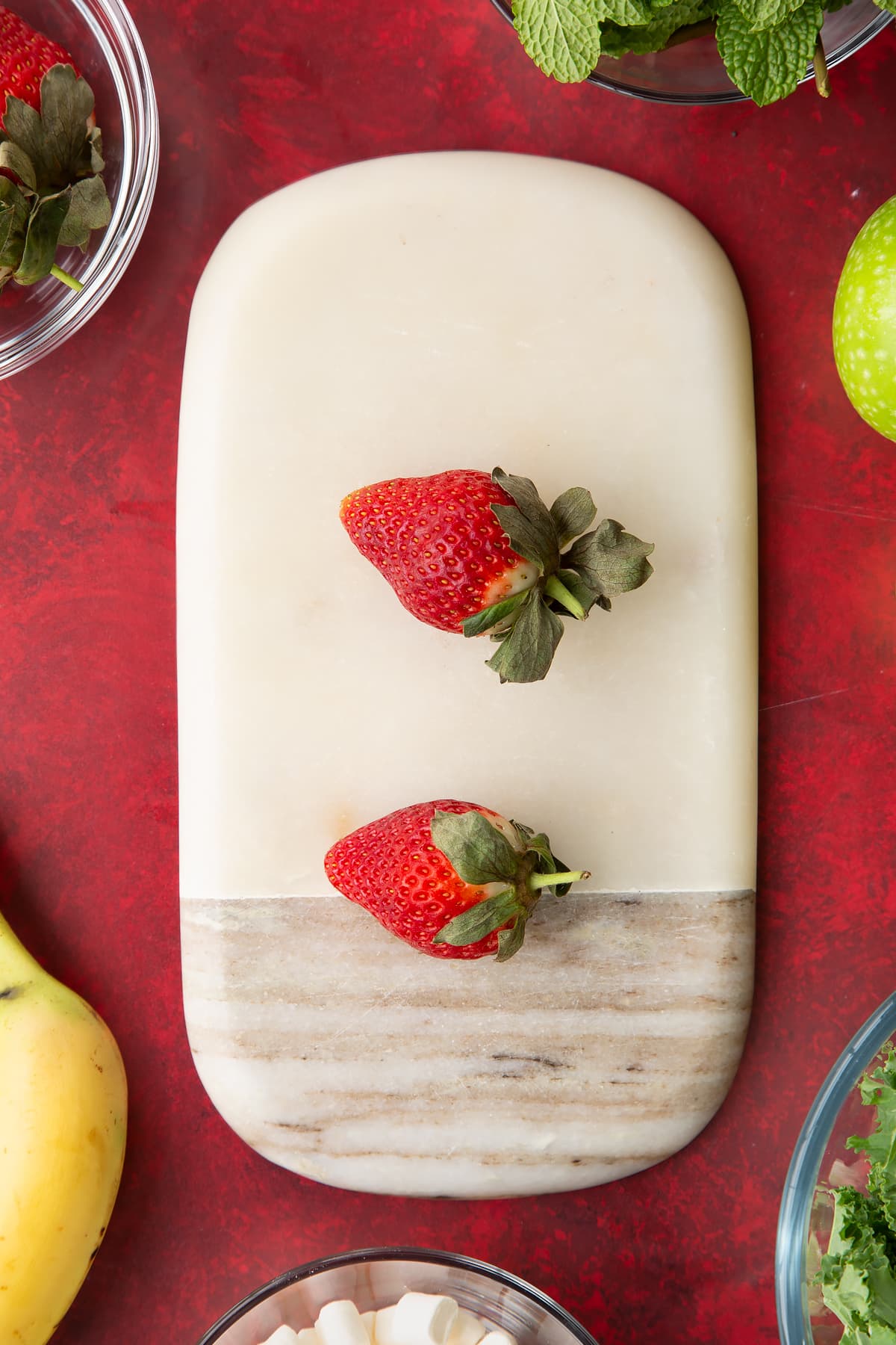 Overhead shot of two strawberries on a decoative board.