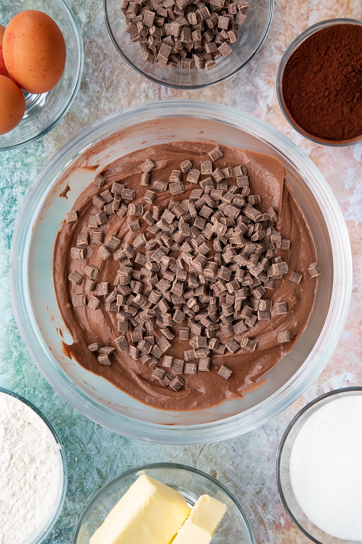 Overhead shot of the mint choc chip cupcakes mixture in a bowl with chocolate chips being added.
