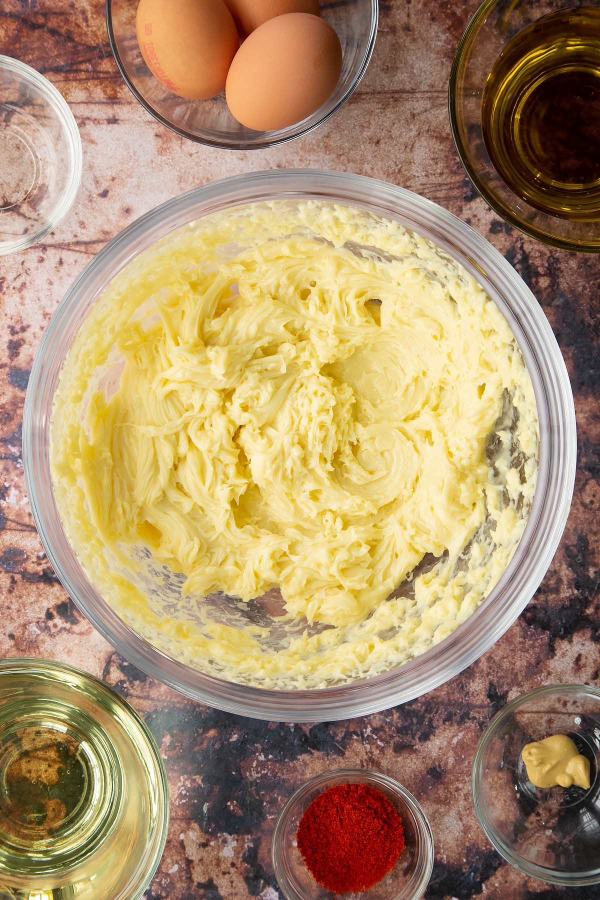 Thick olive oil mayo in a bowl. Ingredients to make paprika mayo surround the bowl.