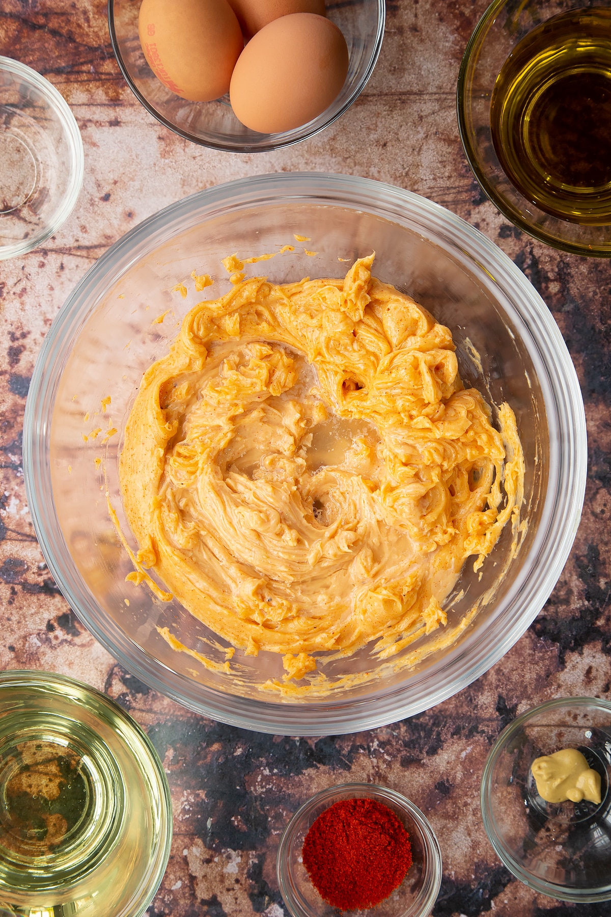 Thick paprika mayo in a bowl with lemon juice on top. Ingredients to make paprika mayo surround the bowl.