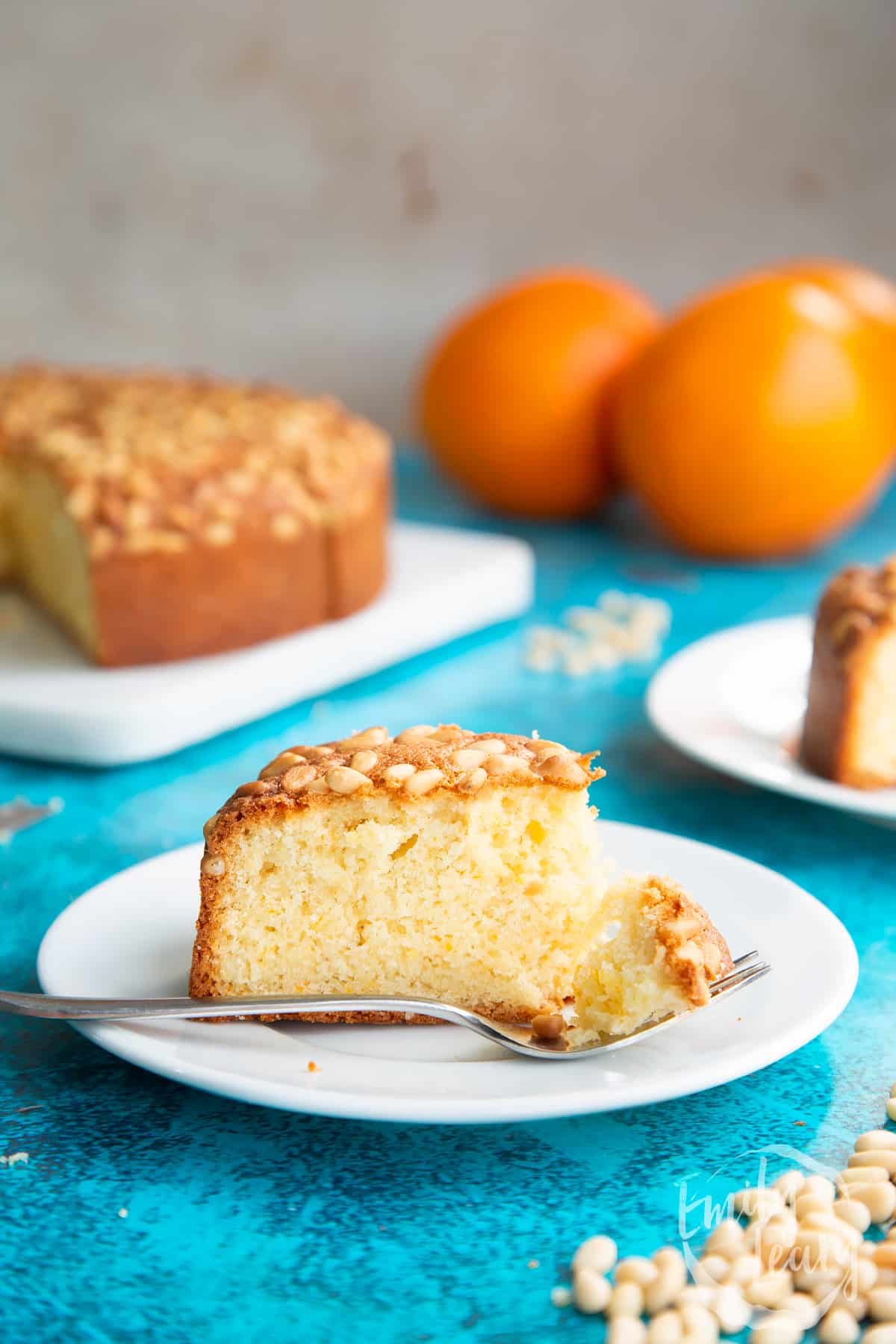 Slice of pine nut cake on a white plate. A fork rests on the plate with a piece of cake on it.