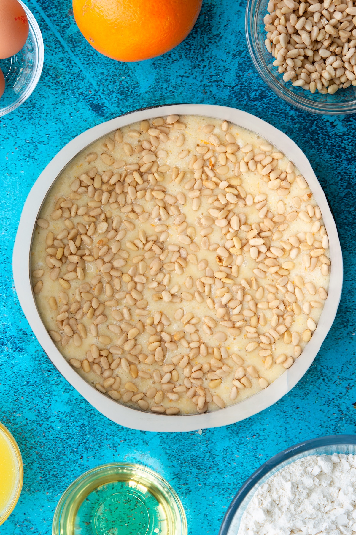 Pine nut cake batter, topped with pine nuts in a lined tin ready to bake.