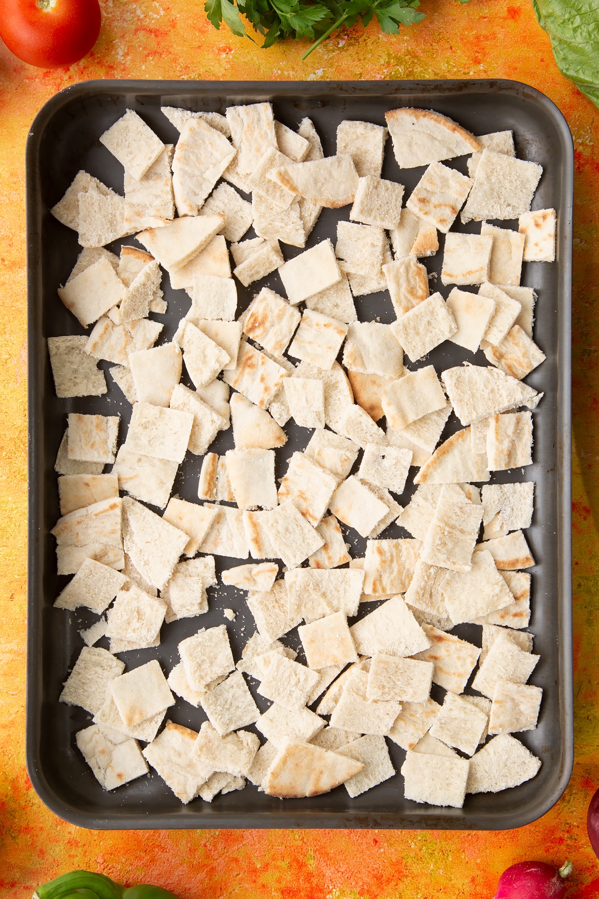 Pitta pieces in a tray. Ingredients to make vegan fattoush surround the tray.