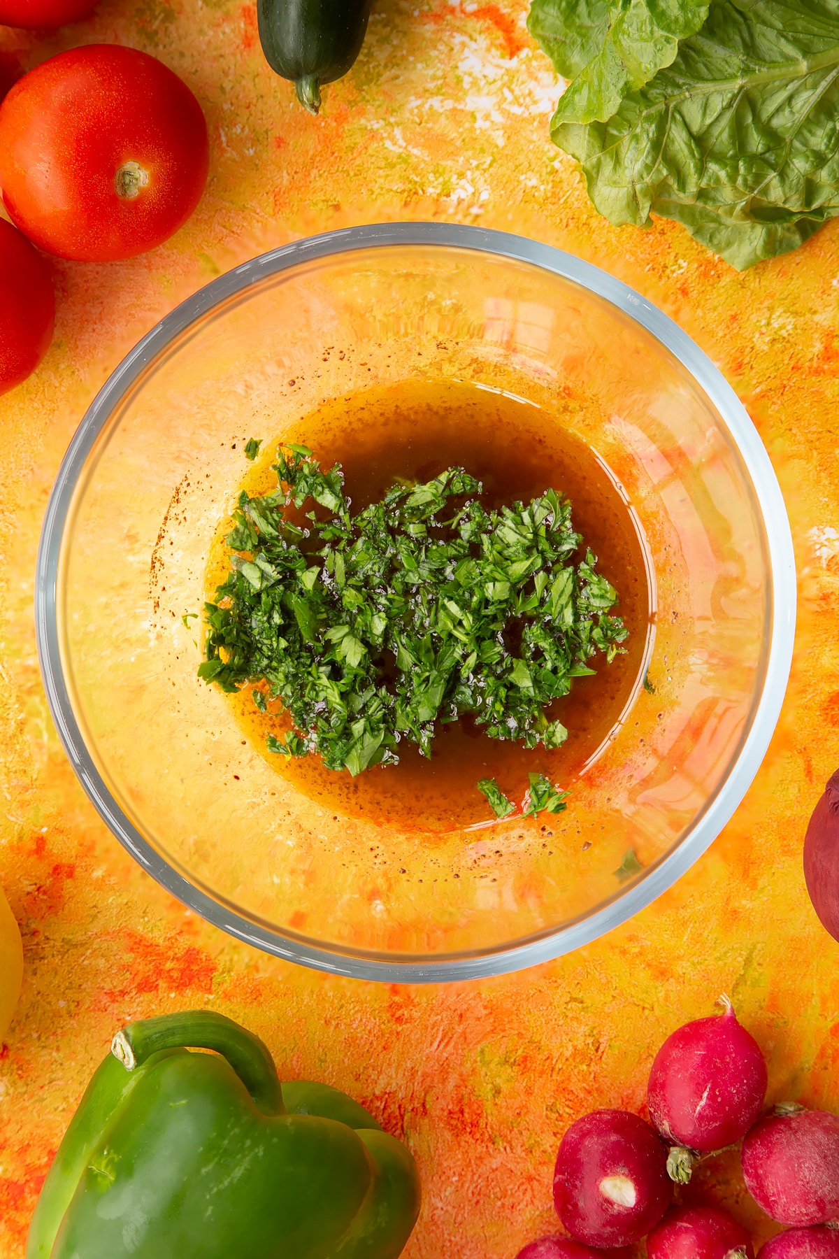 Olive oil, lemon juice, sumac, salt and pepper with parsley on top. Ingredients to make vegan fattoush surround the bowl.
