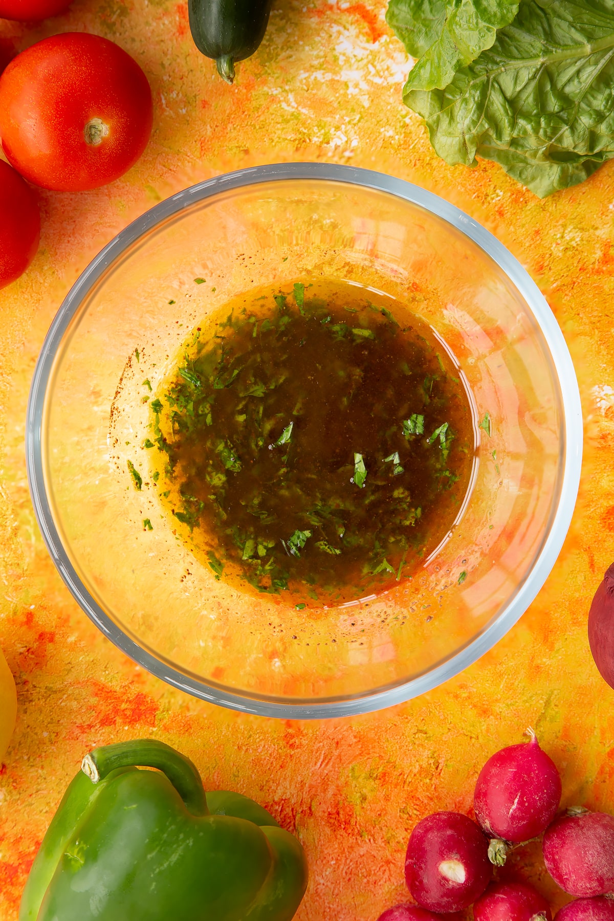 Olive oil, lemon juice, sumac, salt, pepper and parsley whisked together. Ingredients to make vegan fattoush surround the bowl.