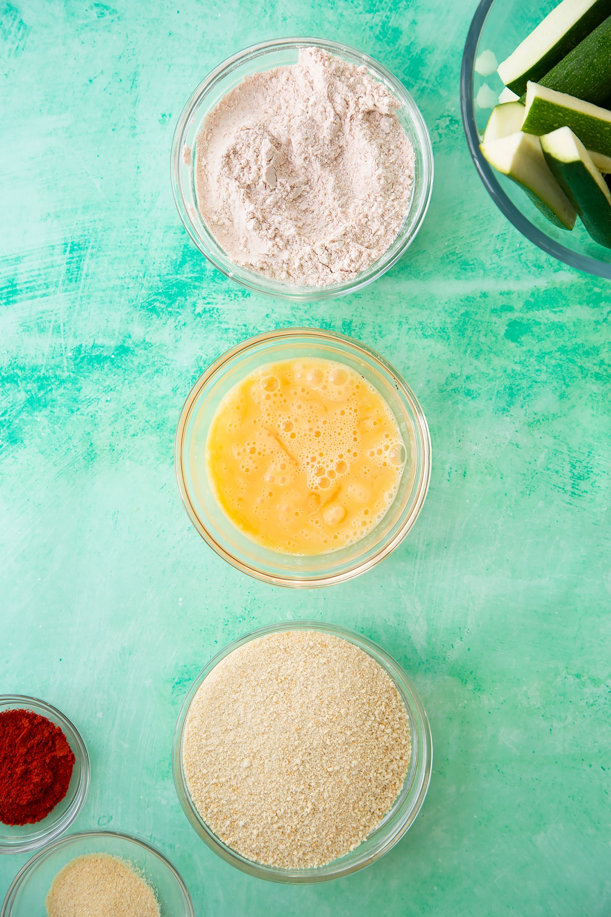 Overhead shot of the three mixing bowls for the baked courgette fries with the flour and spices being mixed together.