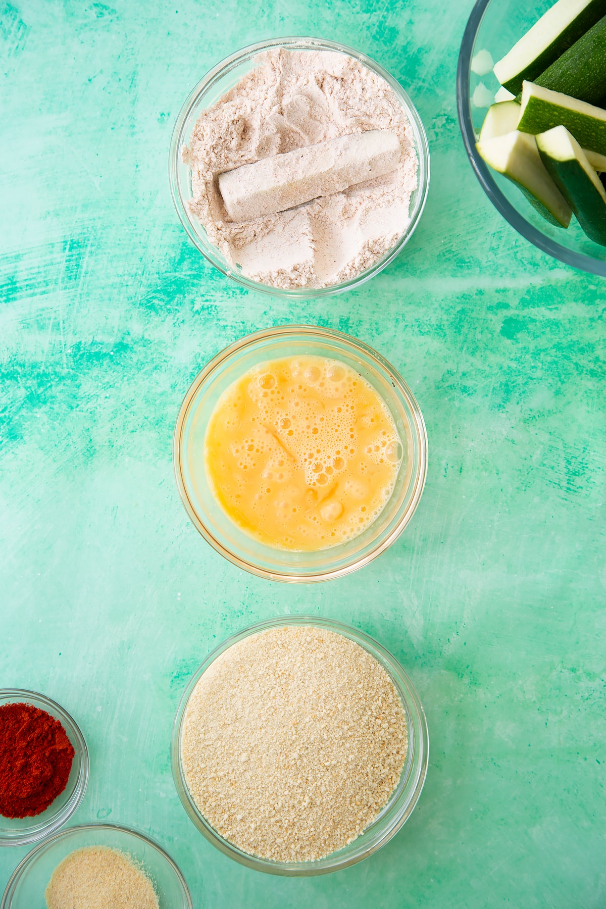Overhead shot of a courgette being dipped in the flour mixture.