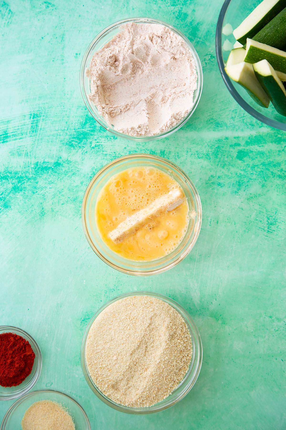 Overhead shot of a courgette being dipped in the egg mixture having been dipped in the flour previously.