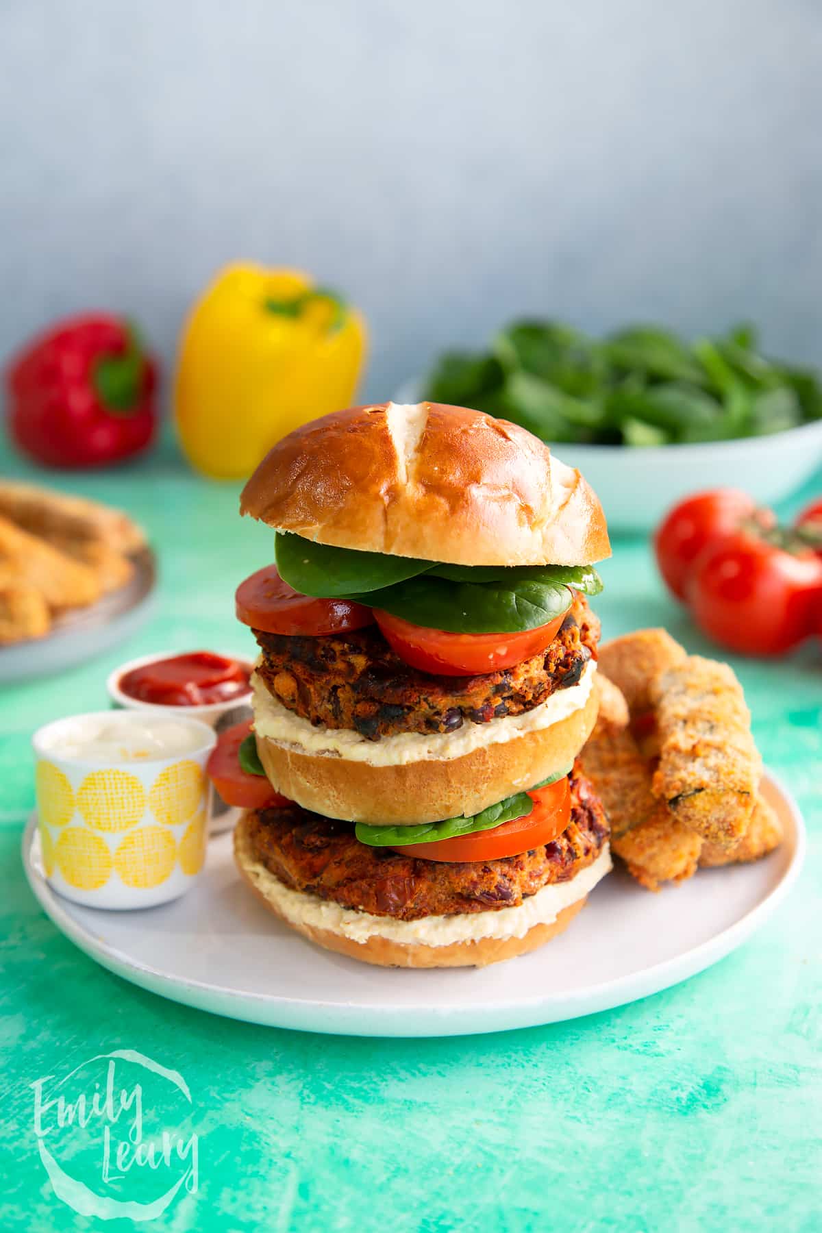 Close up image of a stacked kidney bean burger served on a white plate with dips on the side.