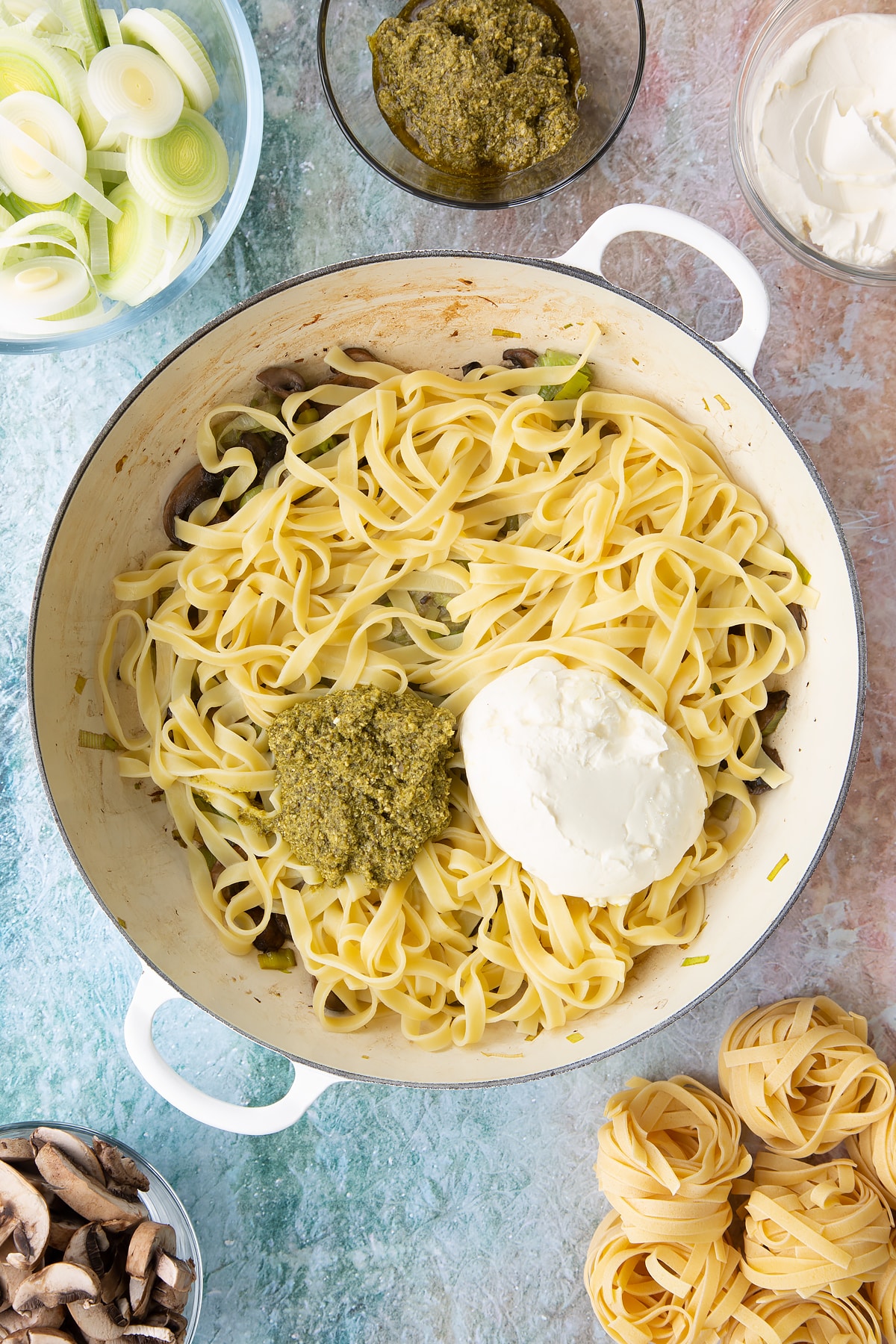 Adding pasta, crème fraîche, pesto to the pan.