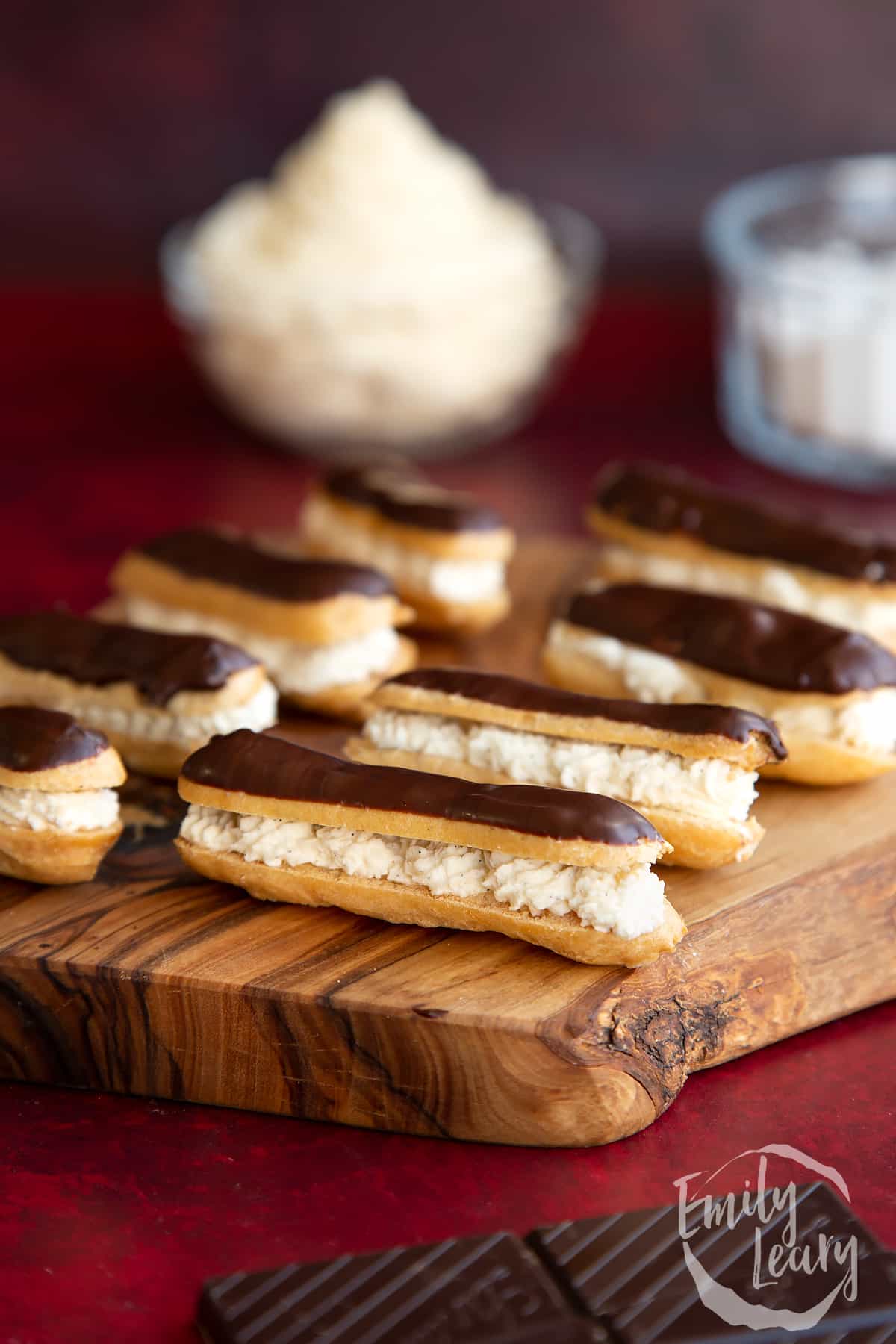 Finished set of mini eclairs served on a wooden board.