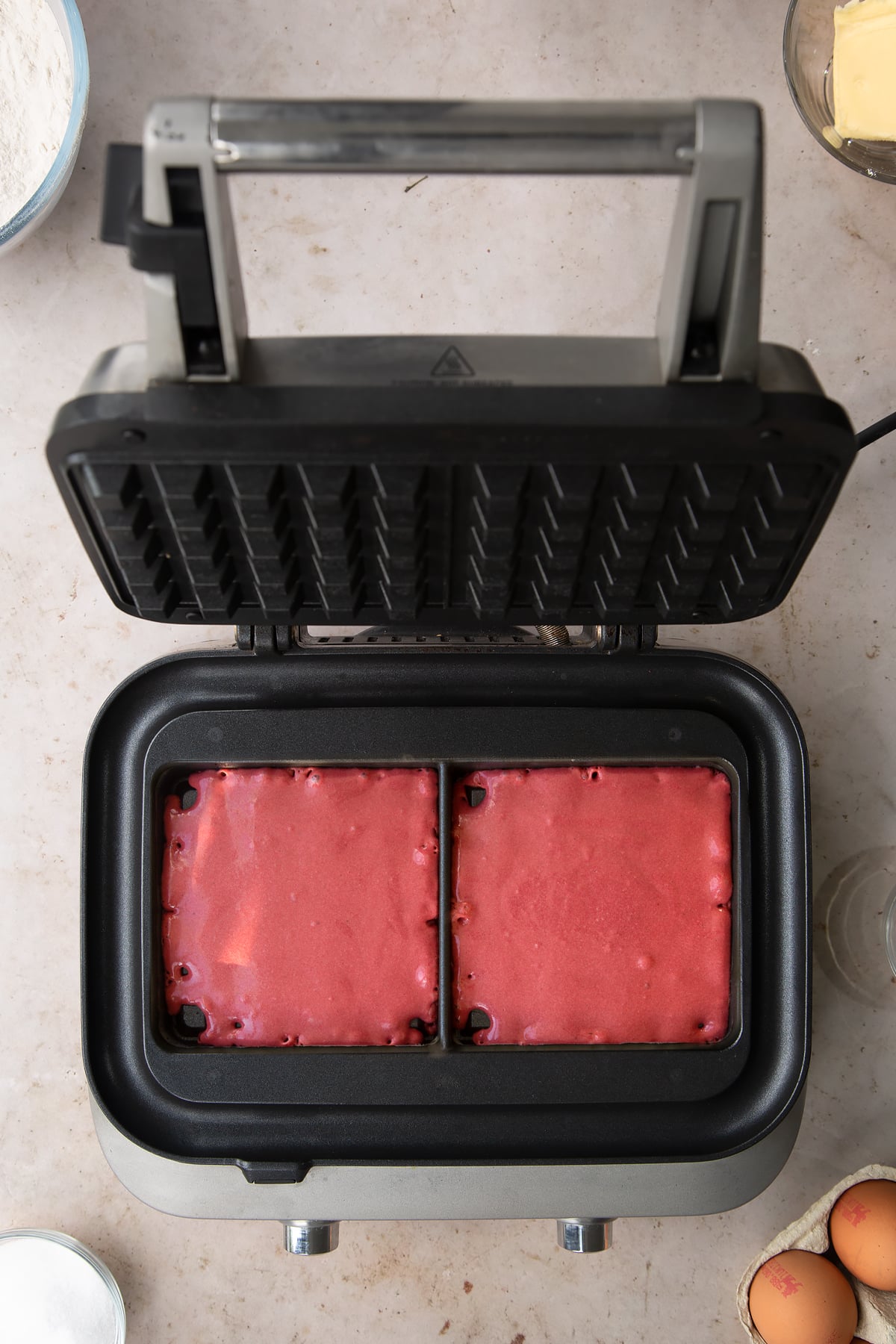 Adding the red velvet waffle mixture to the waffle maker.