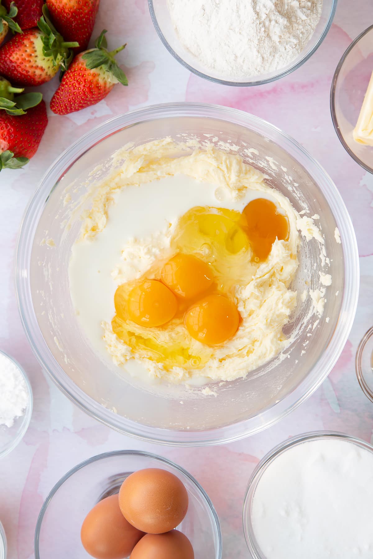 creamed butter and sugar topped with eggs in a large clear bowl with ingredients around the edges