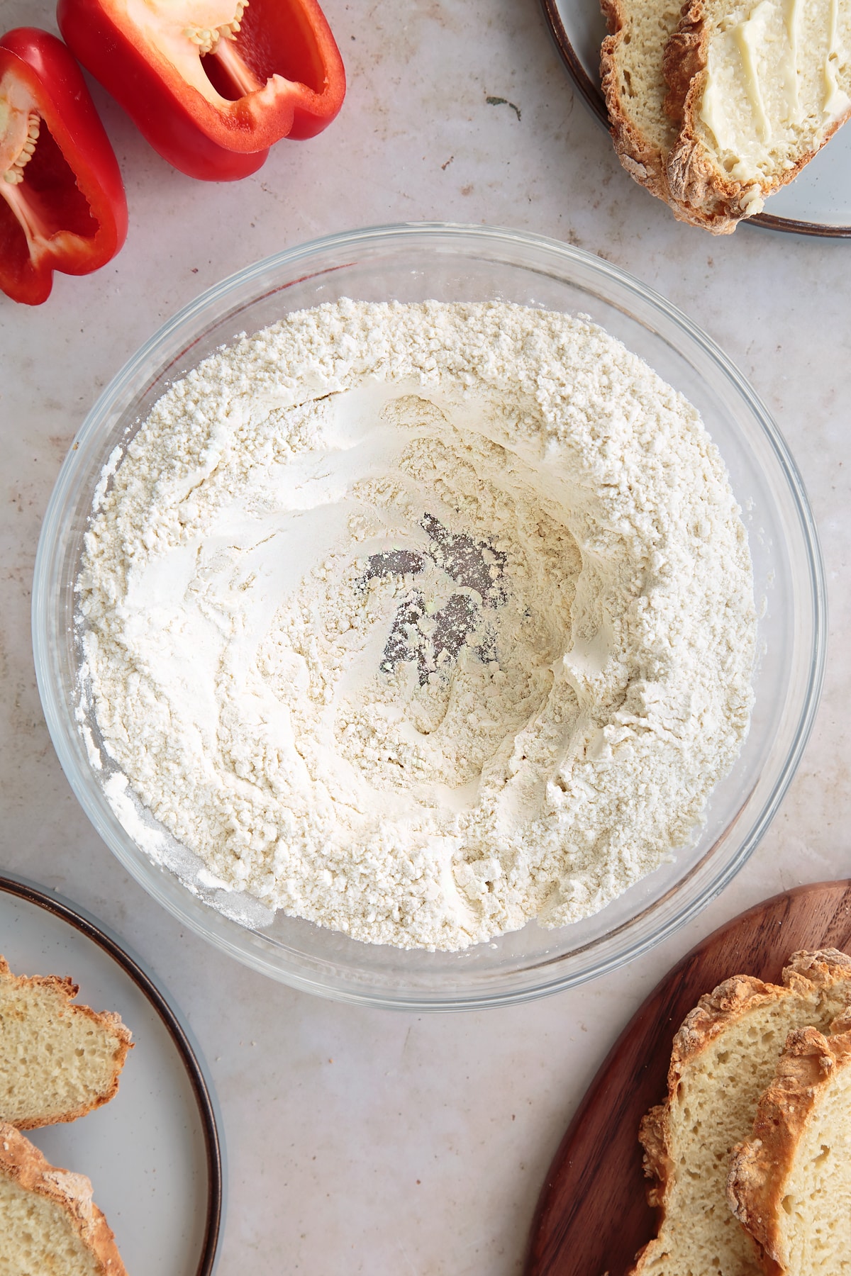 Overhead shot of the spelt flour, salt and bicarbonate of soda in a bowl having been mixed together with a small well in the middle.