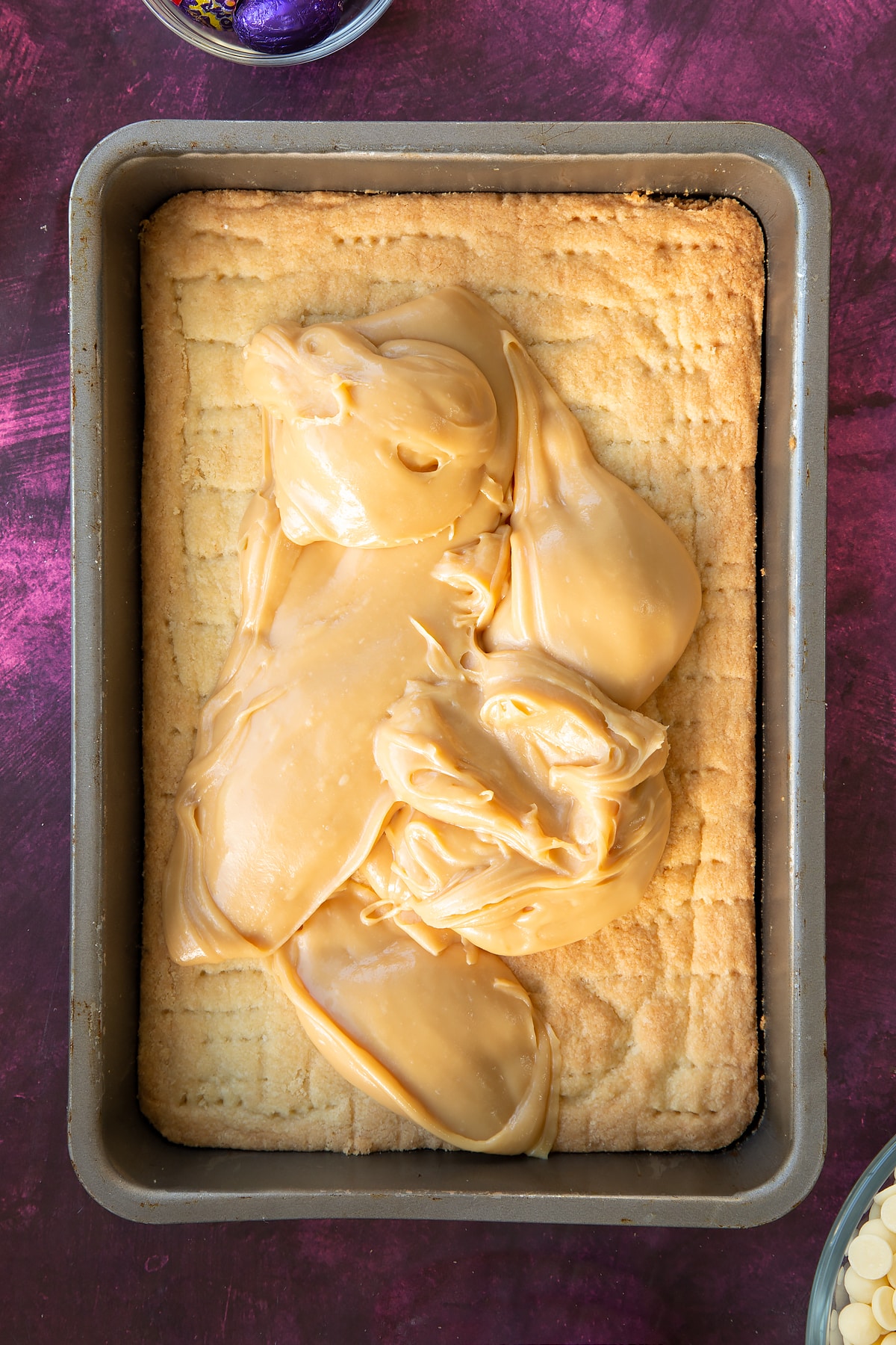 Pouring the caramel over the base layer in a rectangular baking tin.