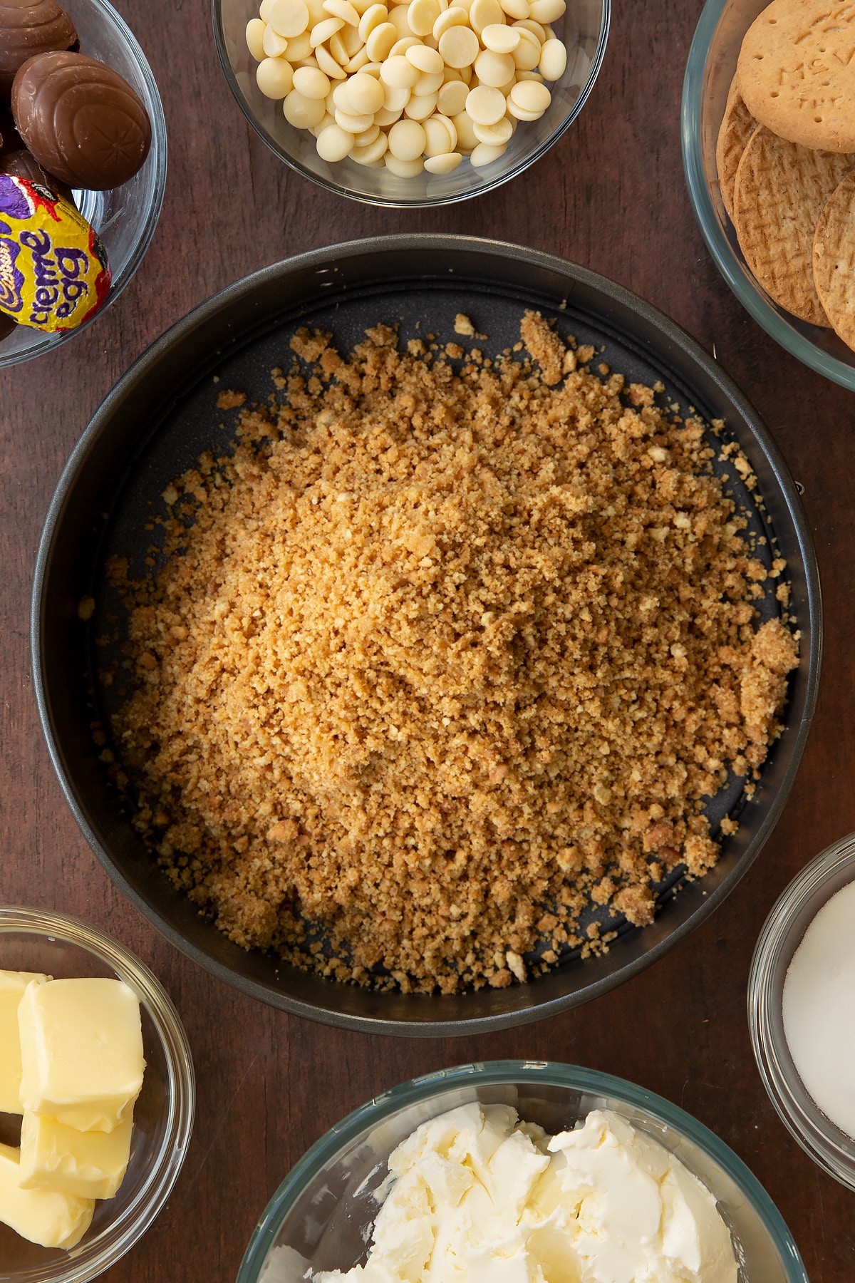 Adding the biscuit mix into a large loose-bottom cake tin.
