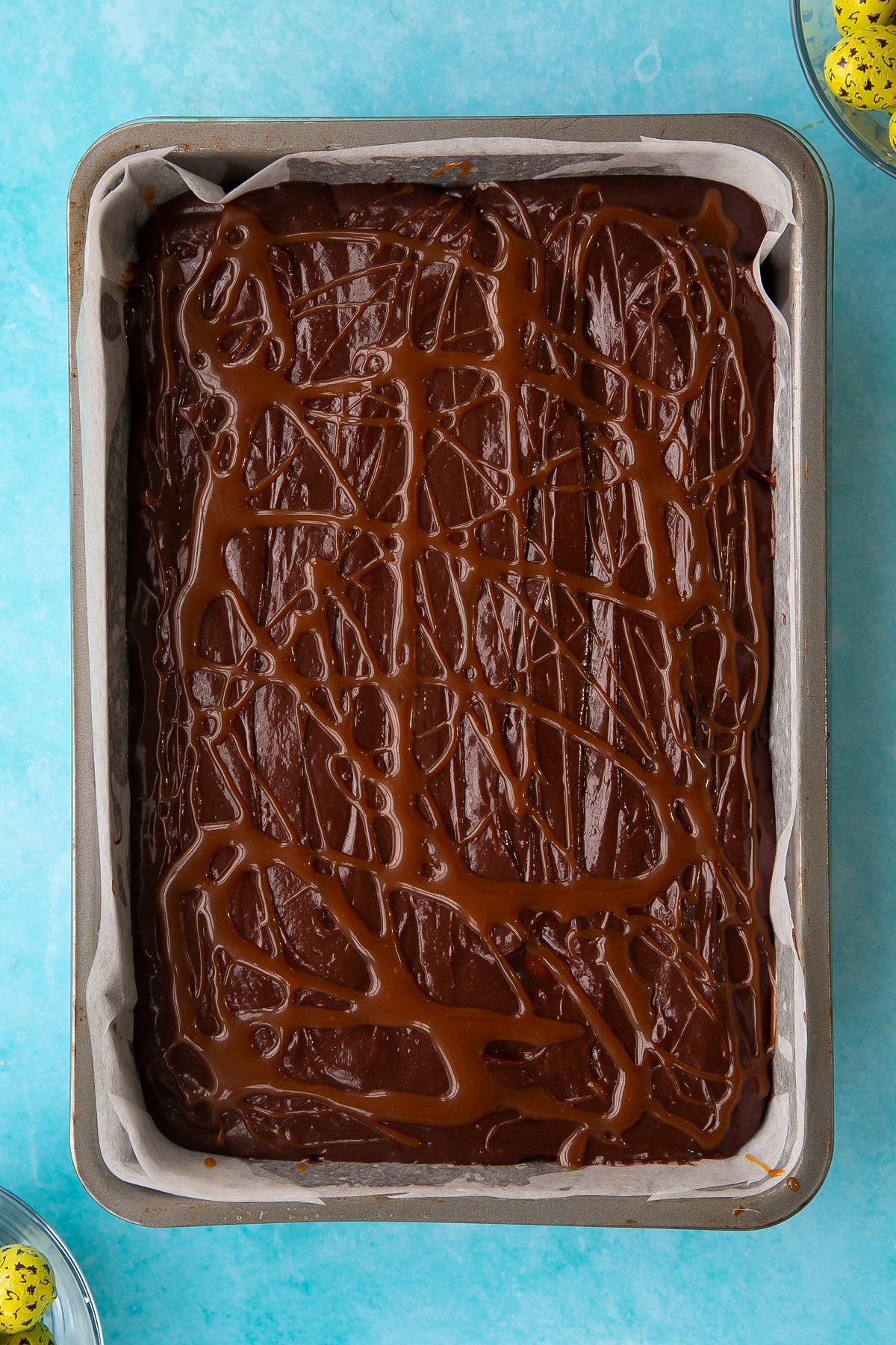 Overhead shot of the caramel being drizzled ontop of the easter brownies wet mixture inside the rectangular cake tin.