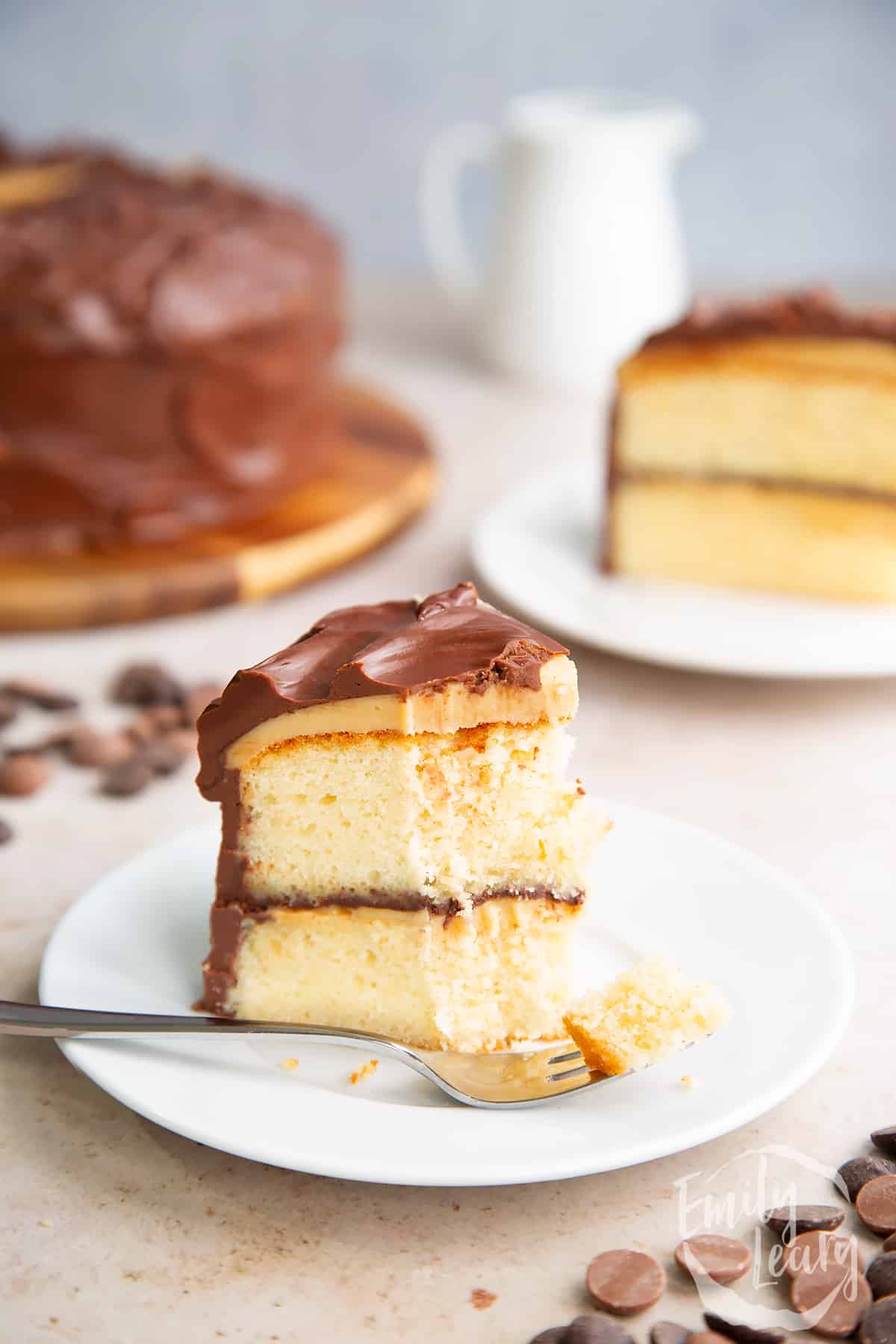 a slice of Millionaire shortbread cake on a white plate with a fork cutting off the front point and the full cake in the background.
