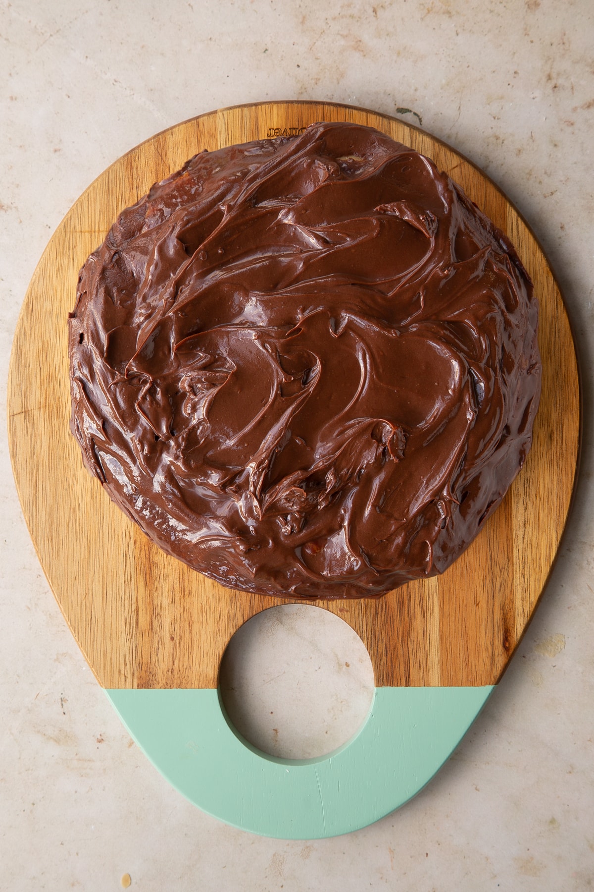 Millionaires sponge cake topped with chocolate ganache on a wooden chopping board.