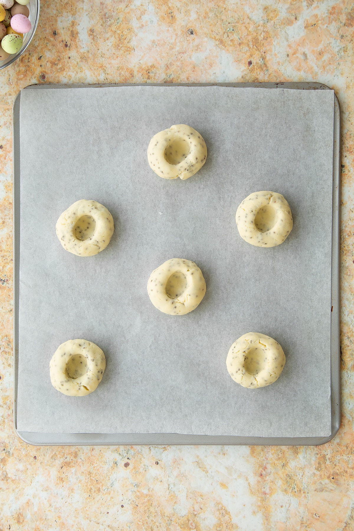 Overhead shot of the biscuits on the baking tray after a thumb has been pressed into each one to create a little well.