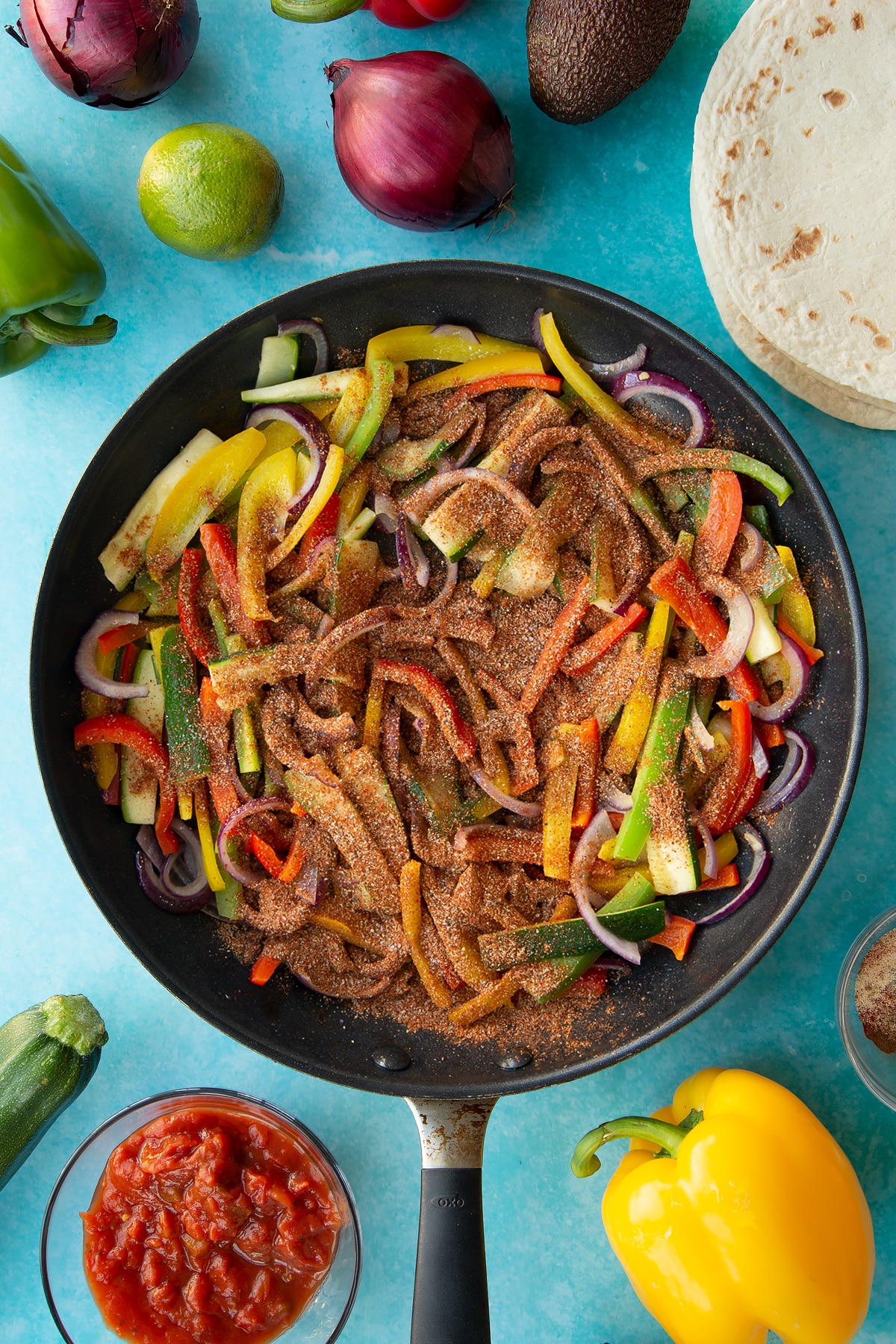 Adding fajita spice to the top of the sliced vegetables in a frying pan.