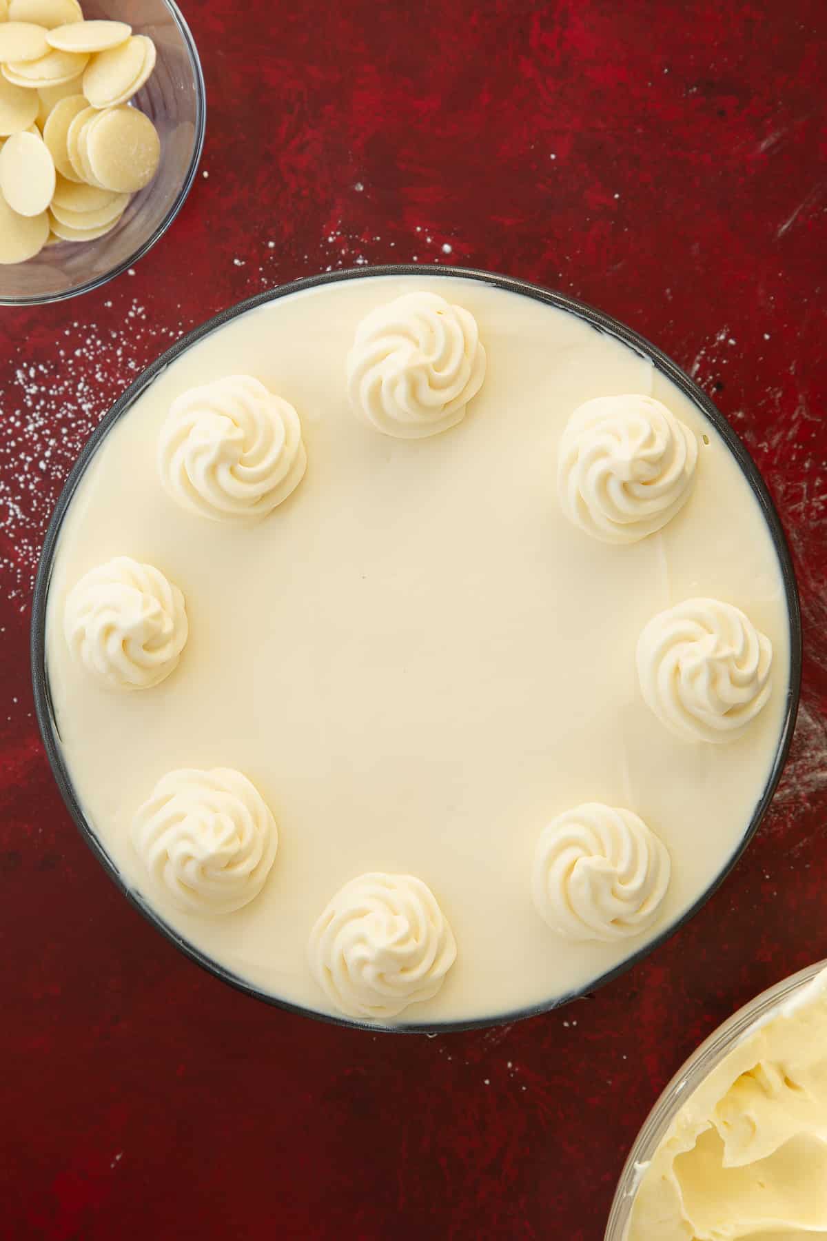white chocolate cheesecake mixture in a round cake tin filled to the top decorated with white chocolate cheesecake rosettes.