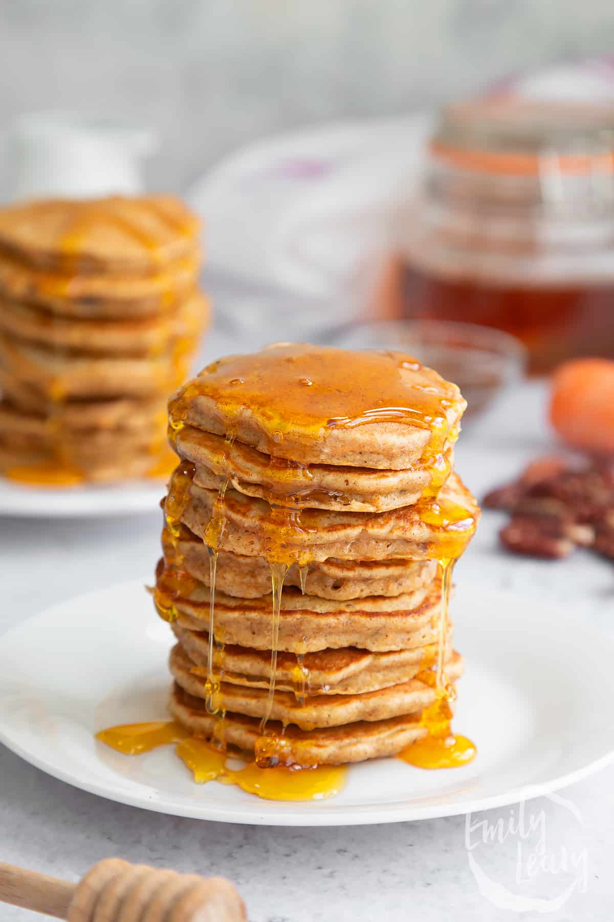 a stack of Carrot cake pancakes on a white plate topped with honey.