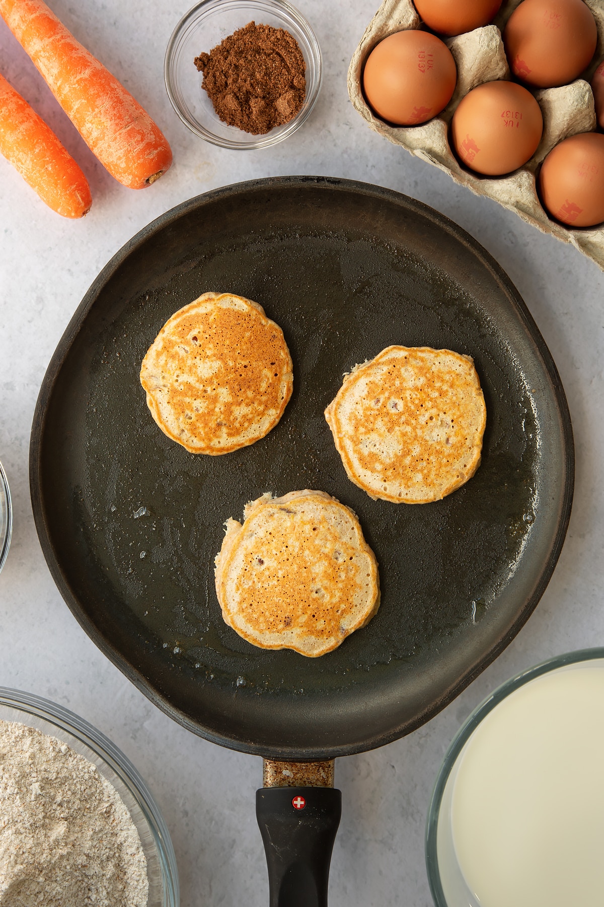 3 carrot cake pancake batter rounds in a large frying pan.