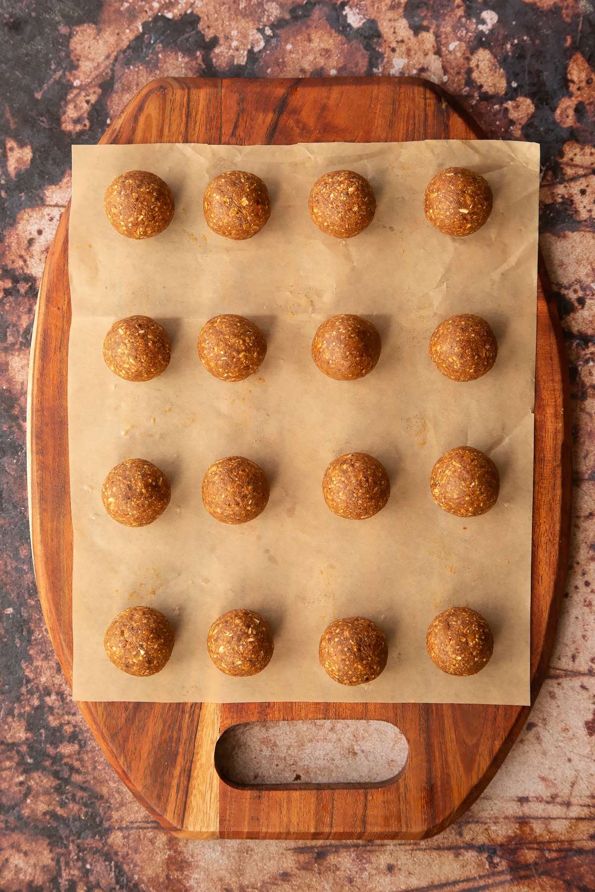 16 small round date energy balls on a parchment lined wooden chopping board.