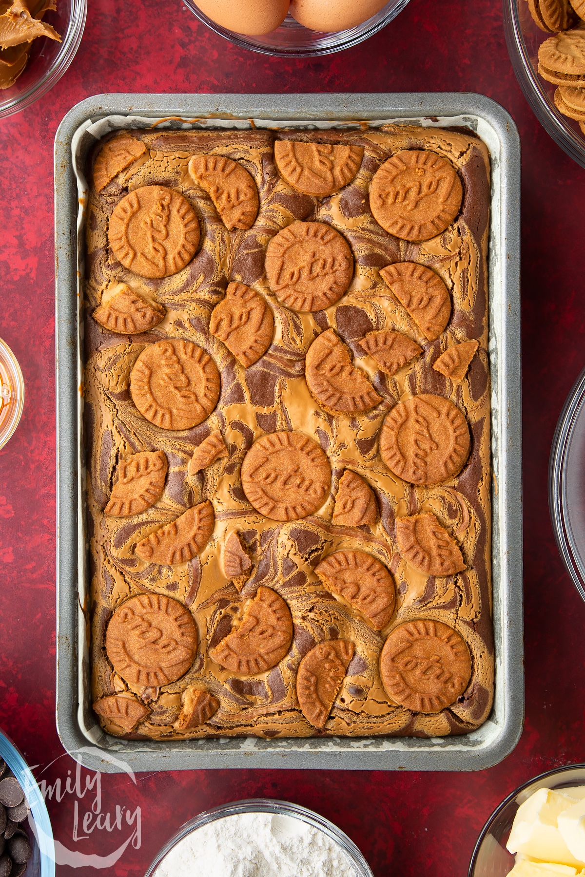 baked brownie batter in a large lined baking tin drizzled with biscoff spread topped with lotus biscuits.