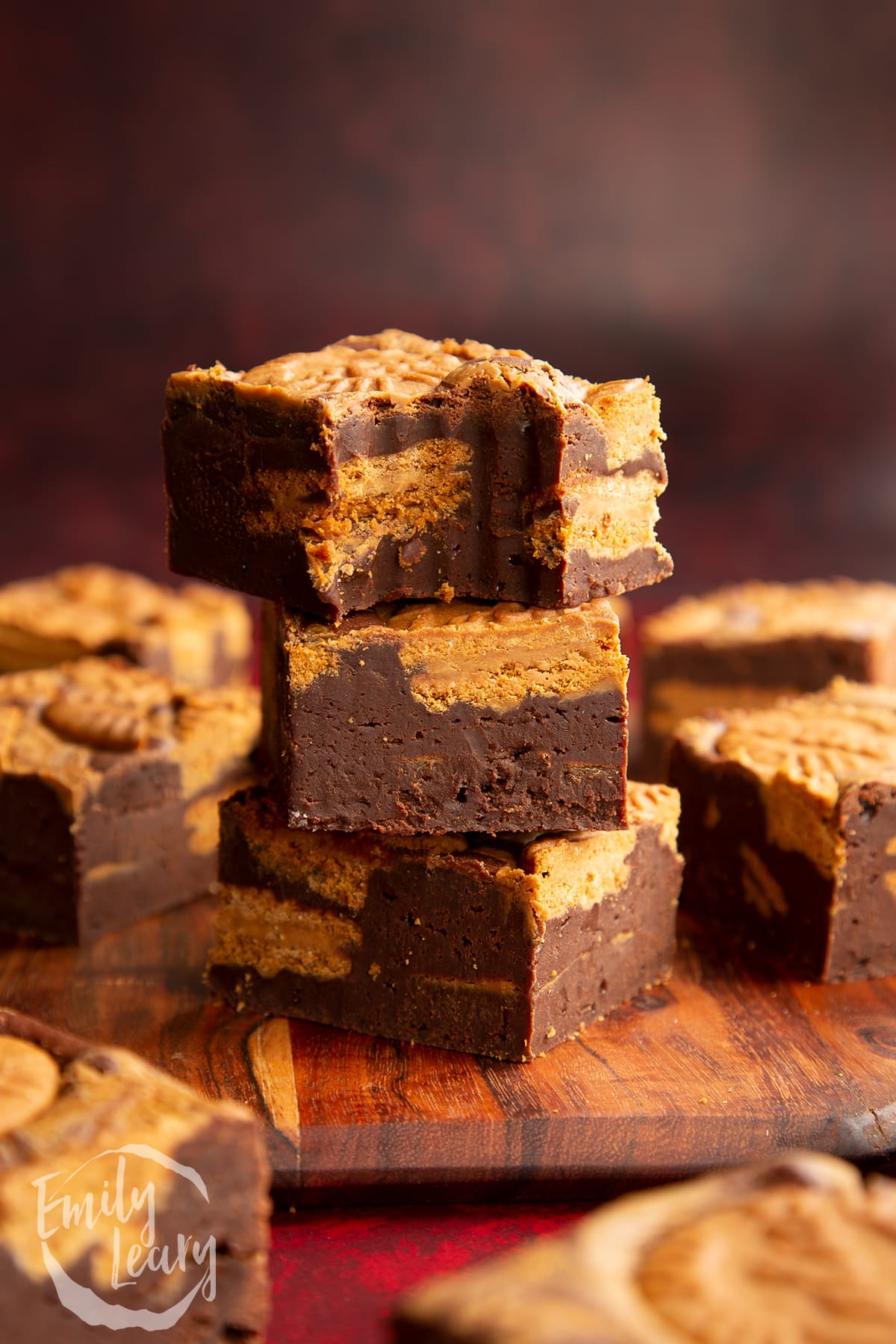 a half eaten Biscoff brownie on top of more Biscoff brownies on a wooden chopping board.