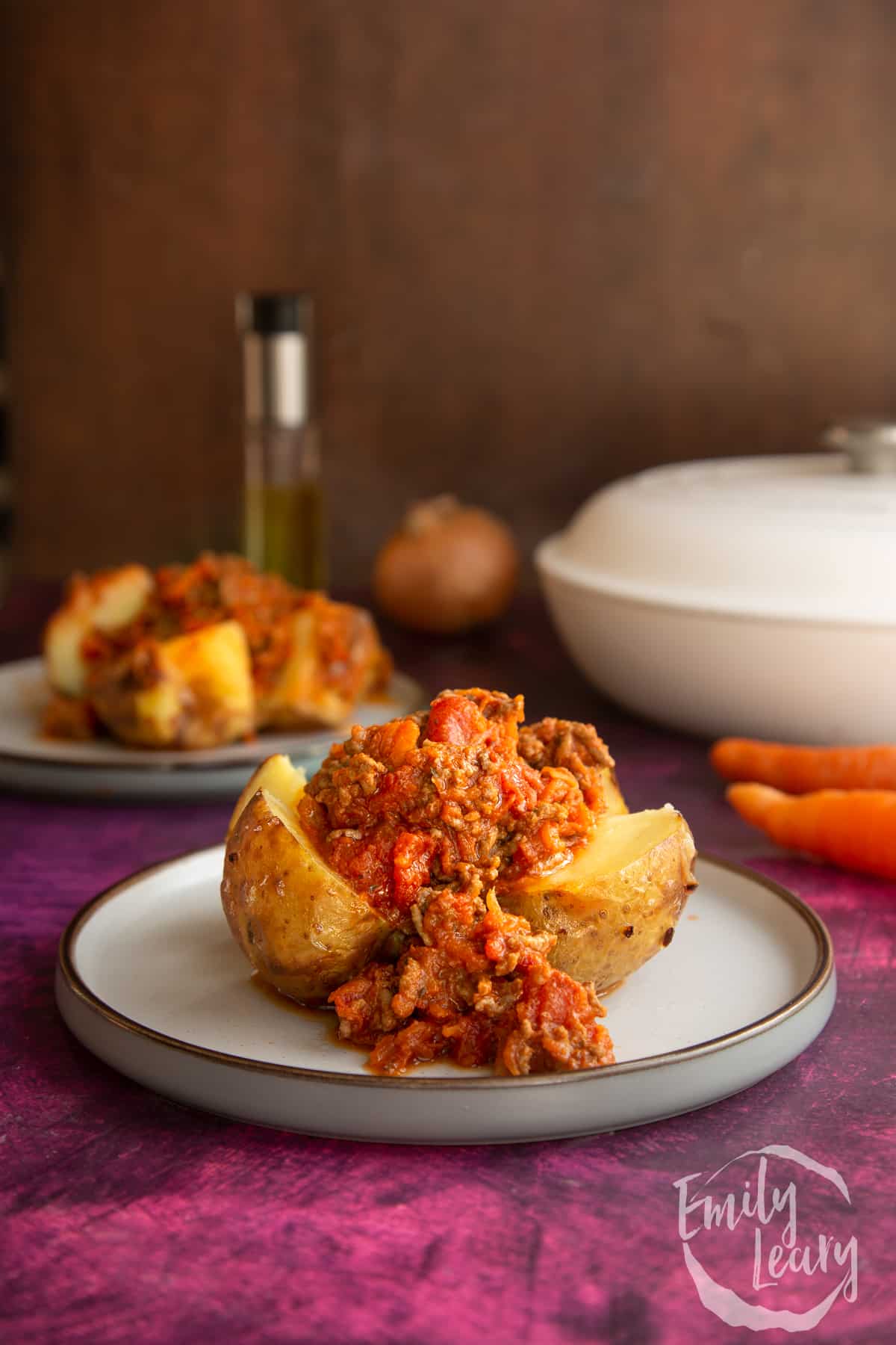a jacket potato cut in half topped with Bolognese sauce on a white plate with ingredients in the background.