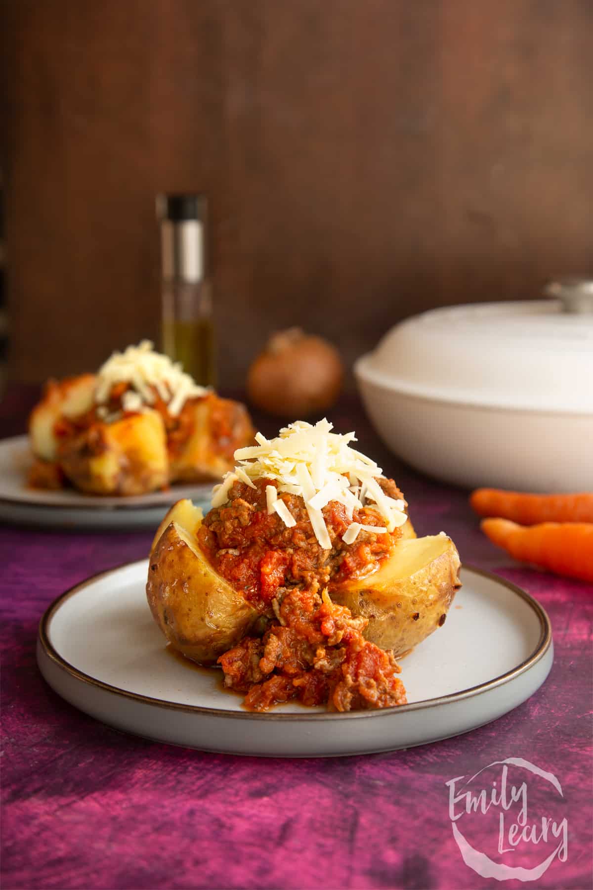 a cooked jacket potato cut in half topped with bolognese sauce and grated cheese on a white plate.