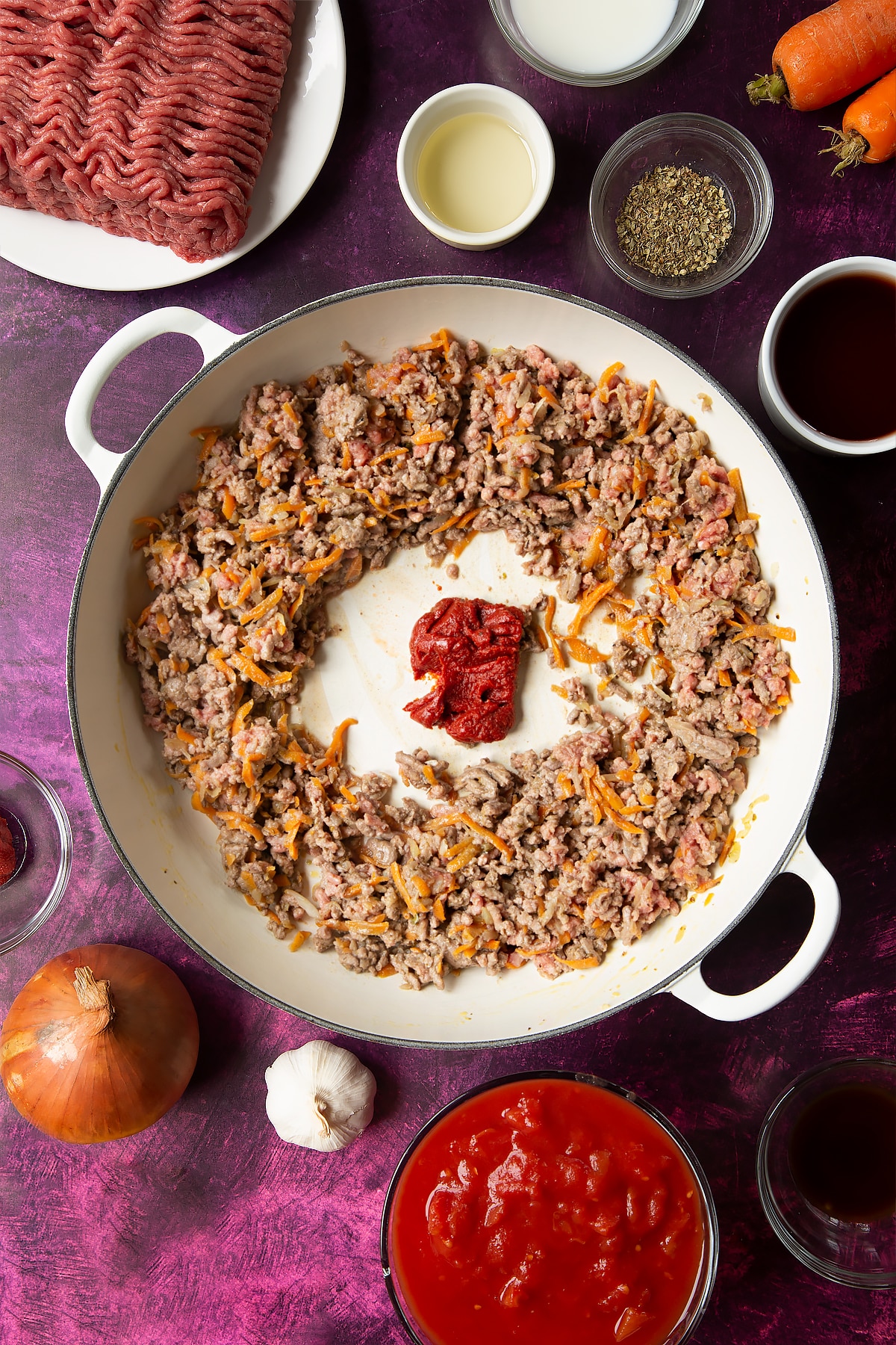 cooked carrot, onion and beef mince mix in a large white frying pan pushed to the edges with a dollop of tomato puree in the middle.