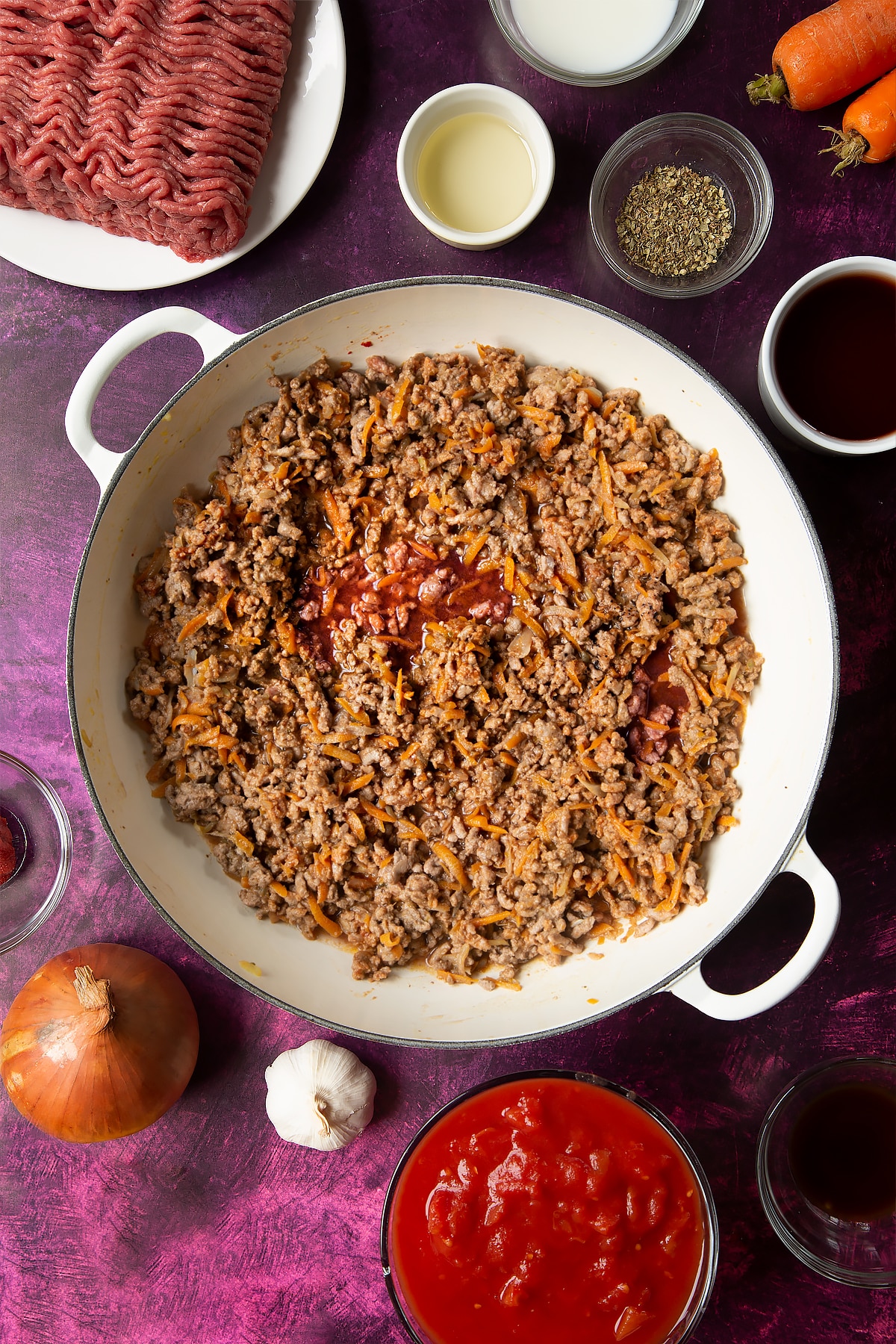 cooked carrot, onion and beef mince mix in a large white frying pan topped with red wine.