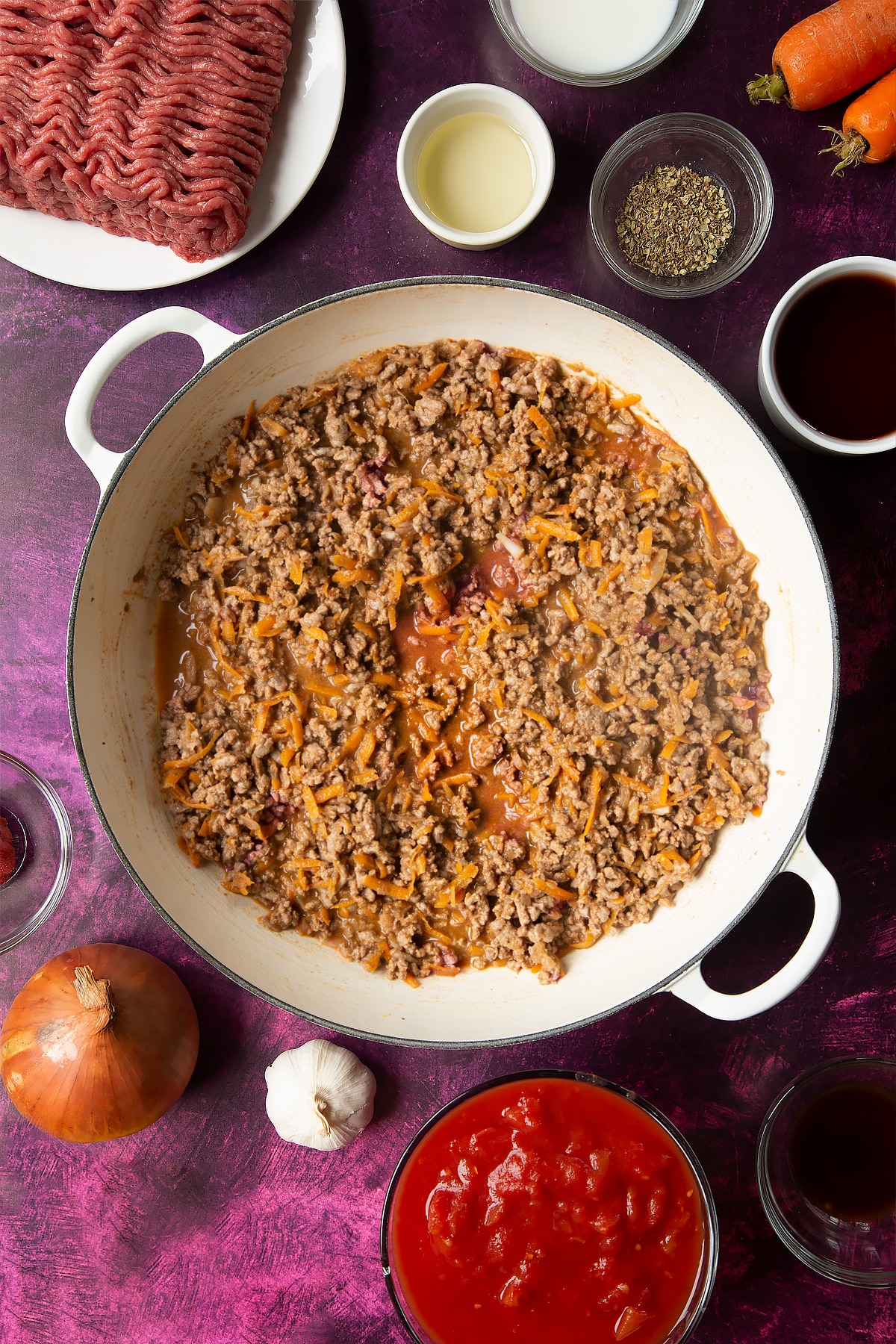 cooked bolognese sauce in a frying pan surrounded by ingredients.