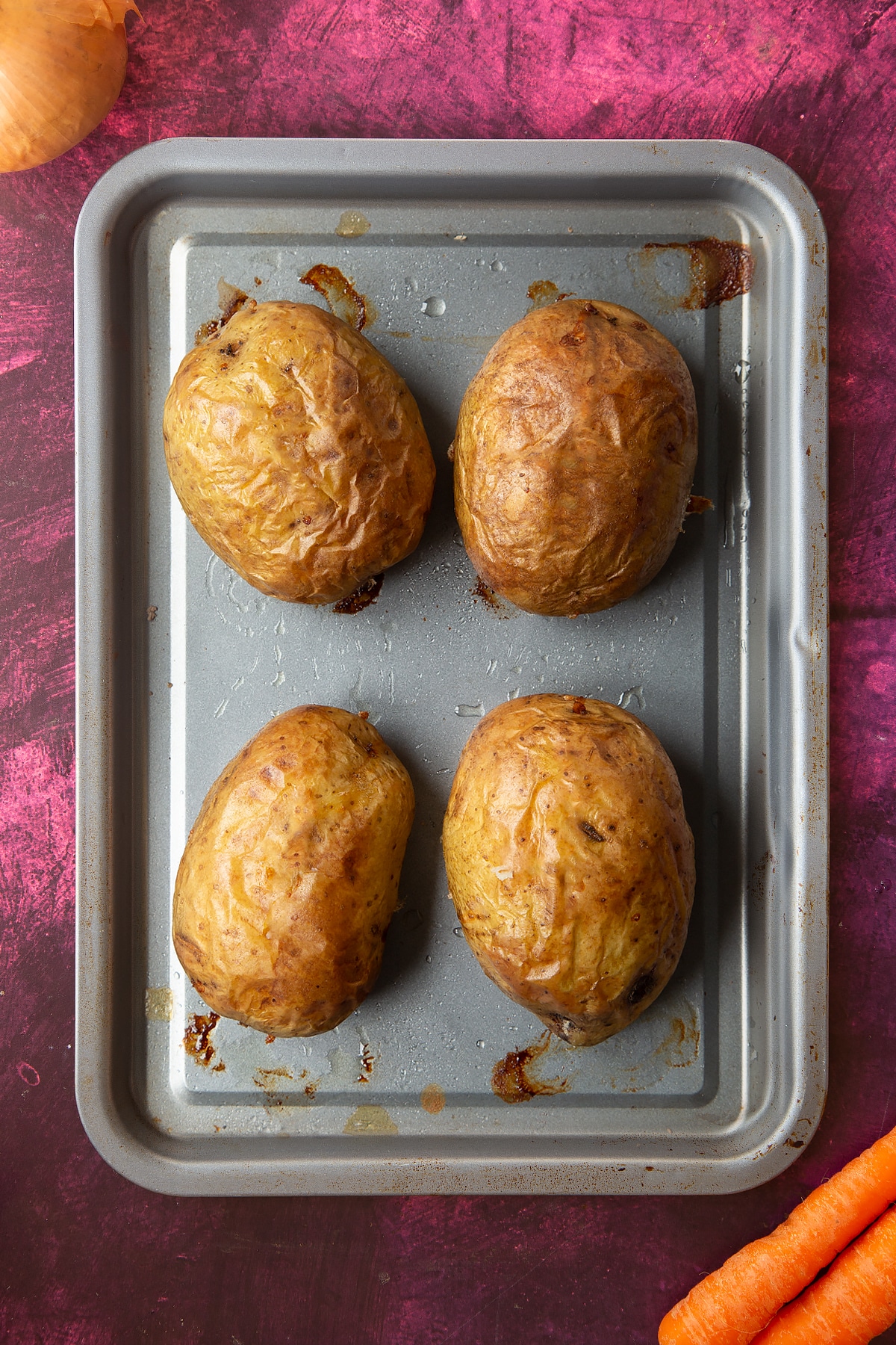 an overhead view of 4 large cooked jacket potatos on a silver baking tray
