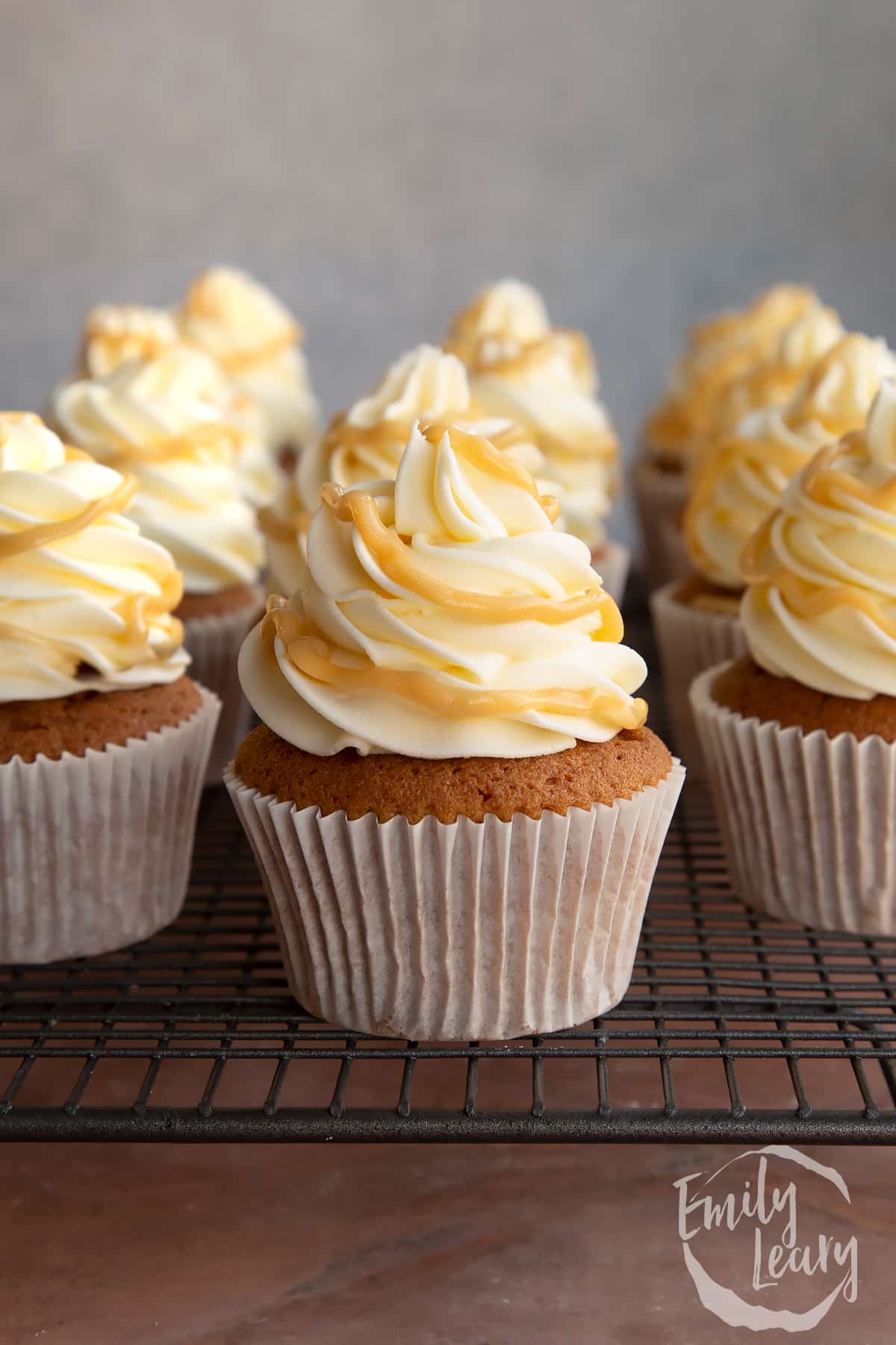 Piped swirls of icing on top of cupcakes on a wire rack drizzled with caramel sauce.