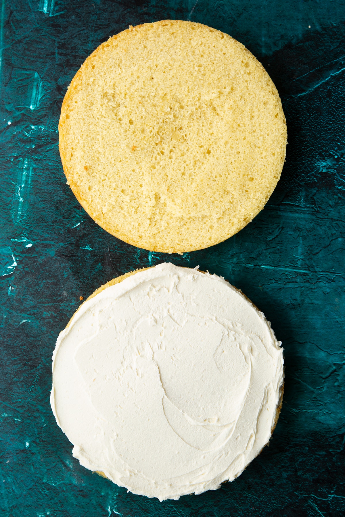 vanilla sponge cake cut in half on a green marble background with one covered in buttercream icing.
