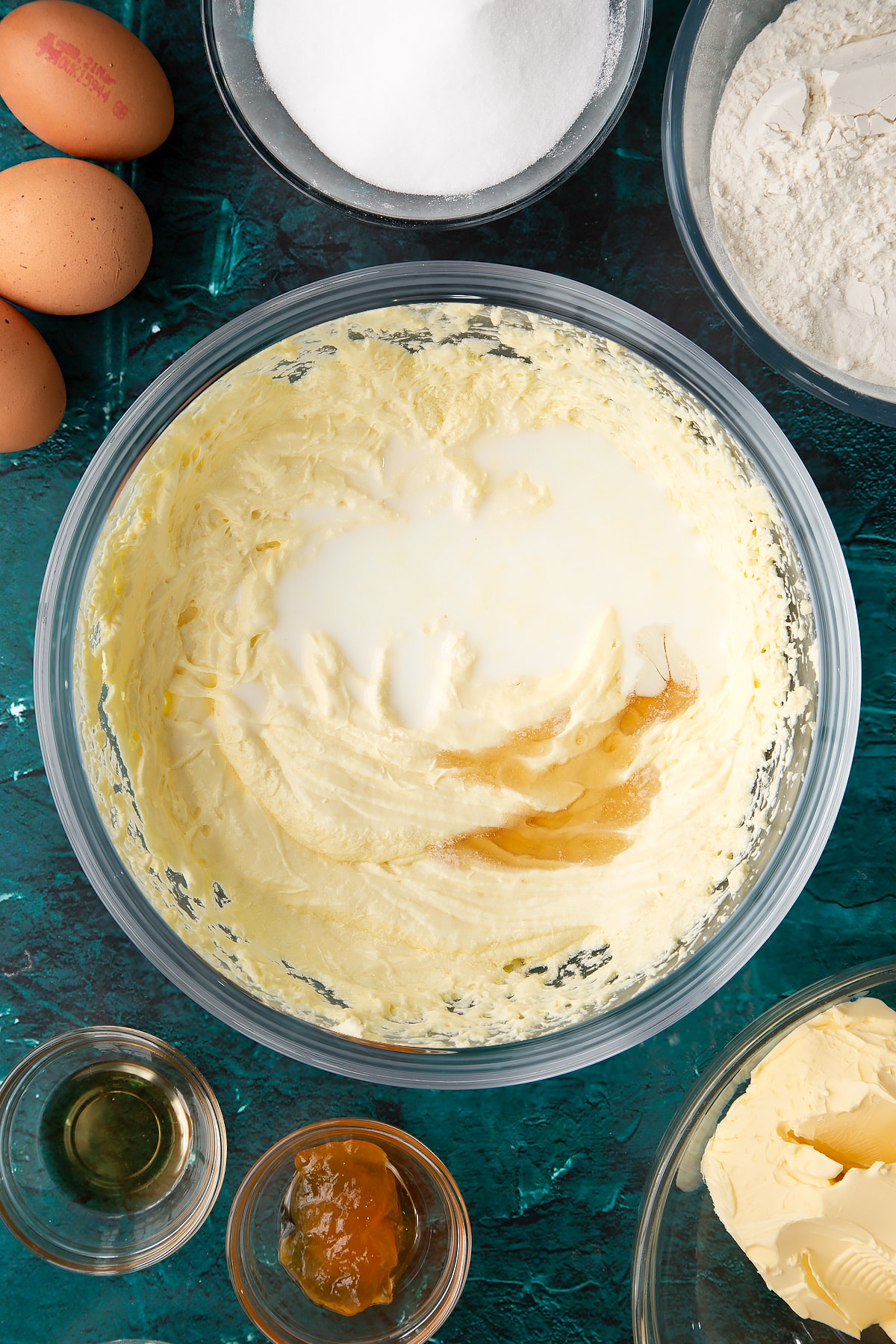 whisked cake batter in a large clear bowl topped with milk and vanilla essence.