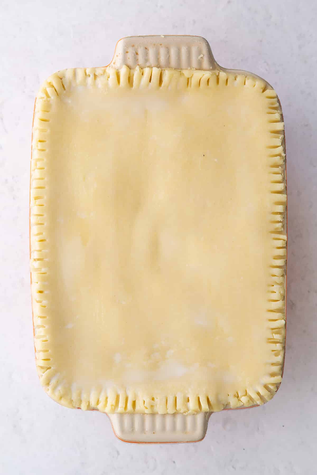 rolled out gluten free pastry pressed to a small roasting dish with ffork style edging and two holes in the middle.