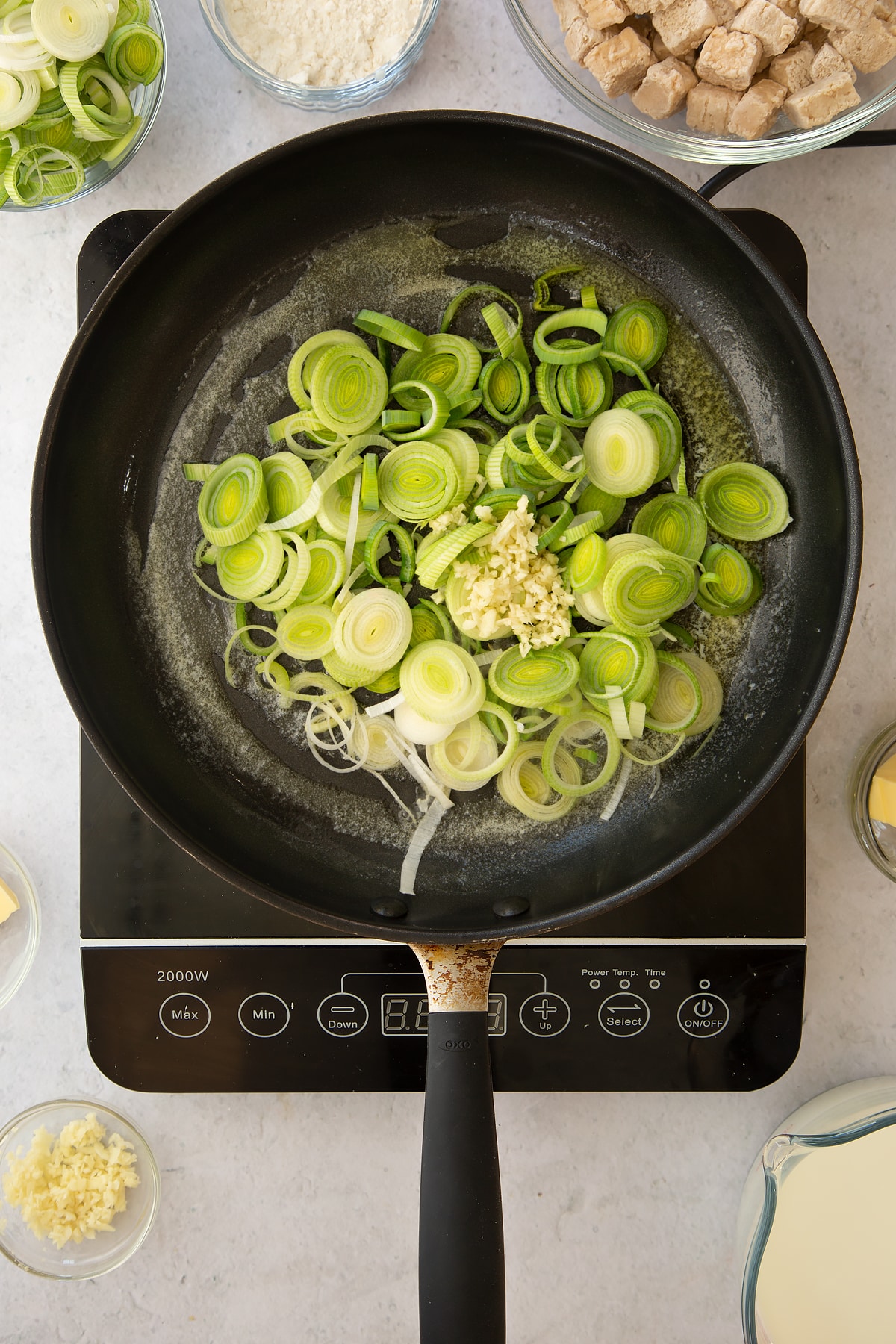 melted butter in a large frying pan topped with sliced leeks and minced garlic.