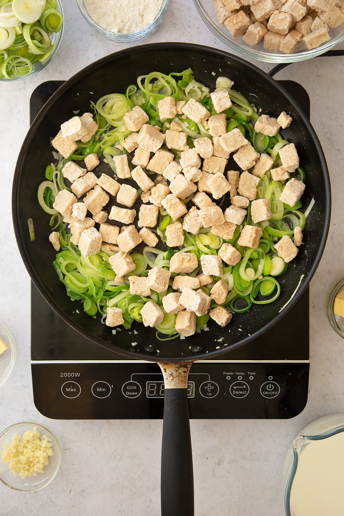 cooked leeks topped with vegetarian chicken-style pieces in a large frying pan on an induction hob.