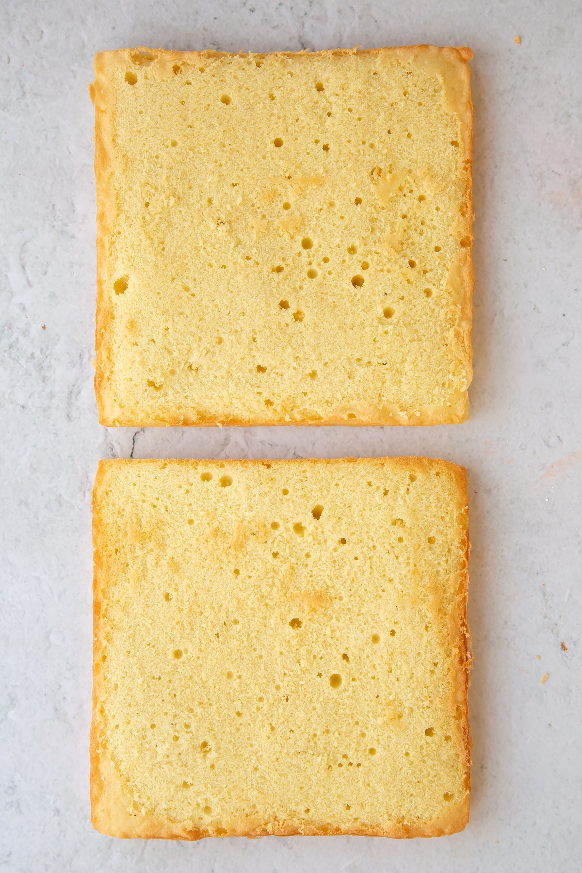 Two square sponge cakes on a marble board.